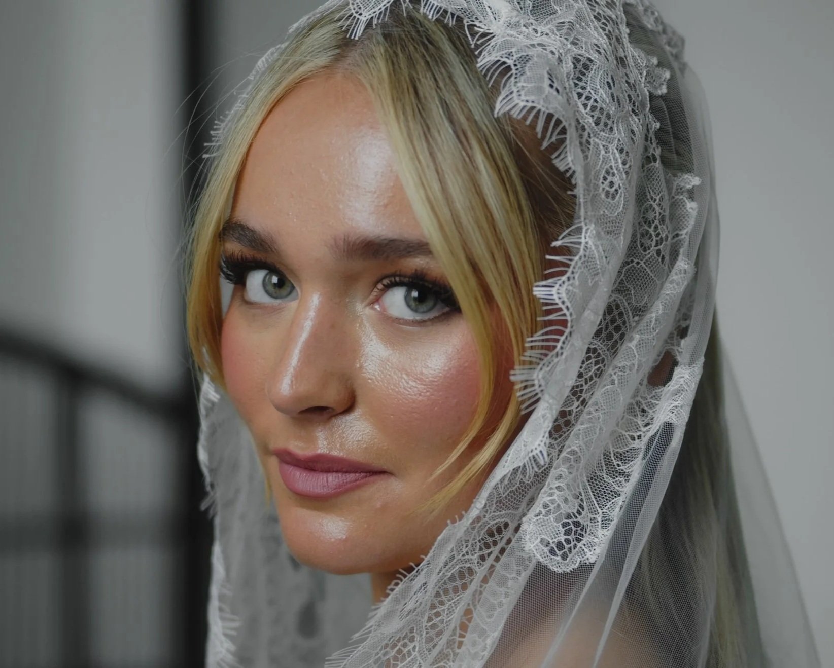 A woman with blonde hair and blue eyes wearing a lace bridal veil.