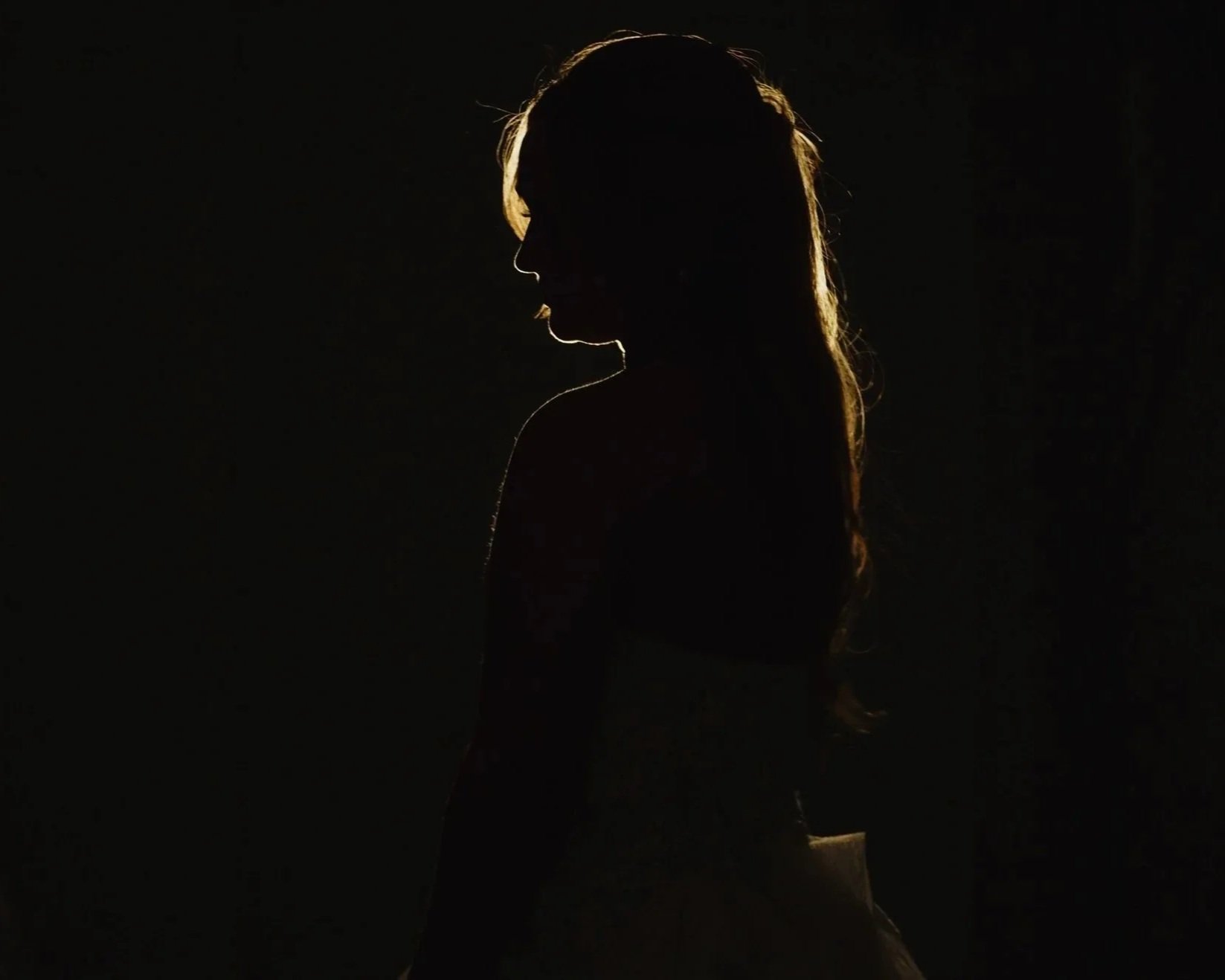 Silhouette of a woman with long hair, backlit to create a glow outline around her head and shoulders, dark background.