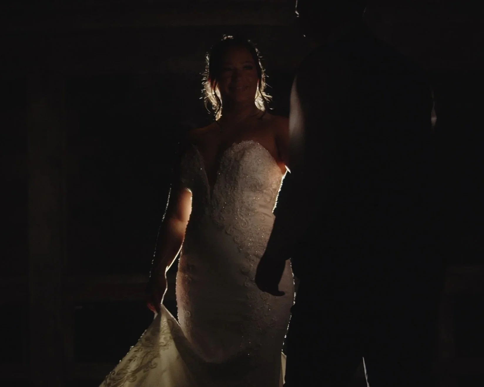 A woman in a wedding dress standing next to a man in a dark suit in a dimly lit environment.