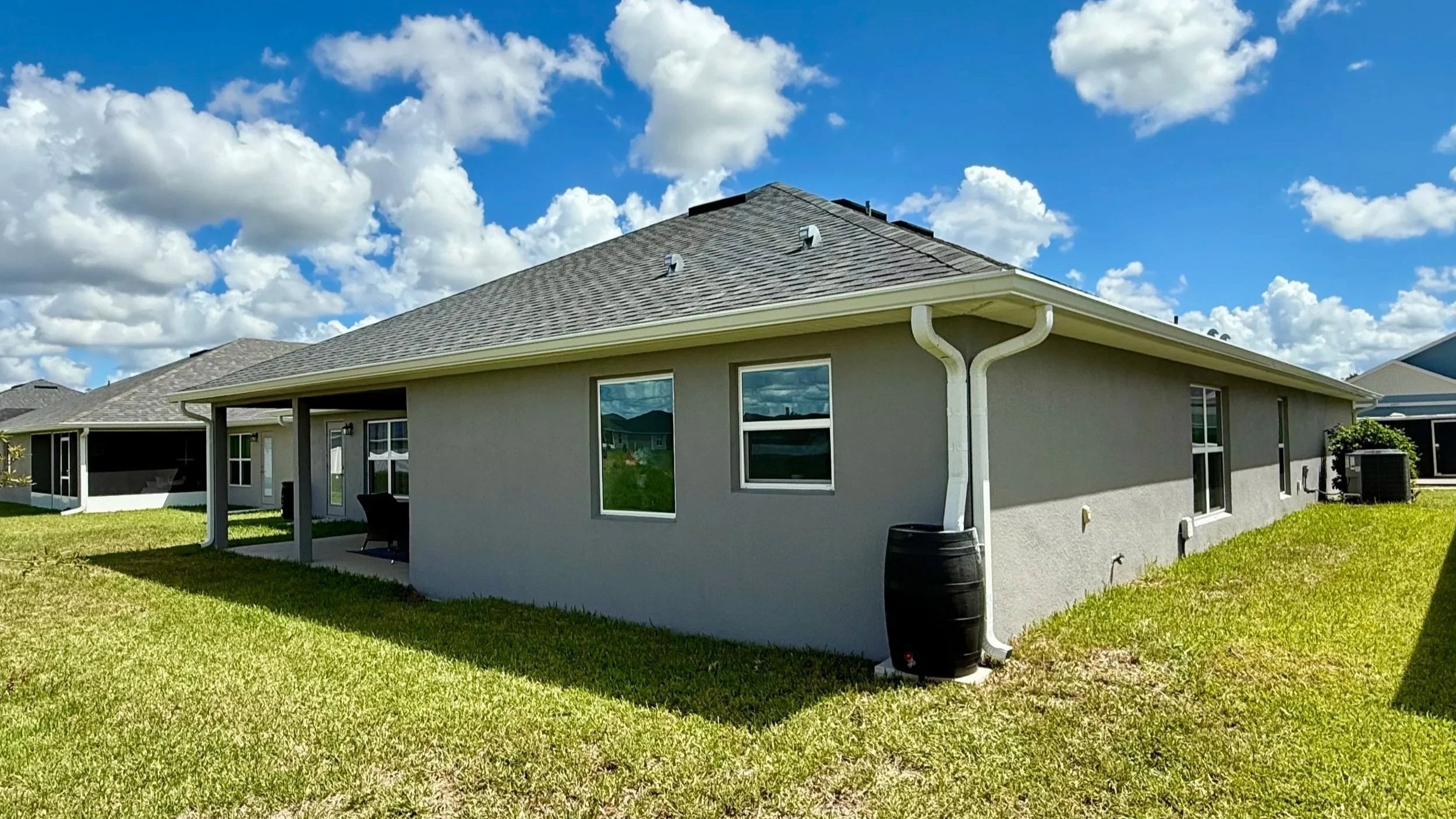White seamless gutters and downspout connected to a rain barrel on a home in Citrus Springs, Florida.