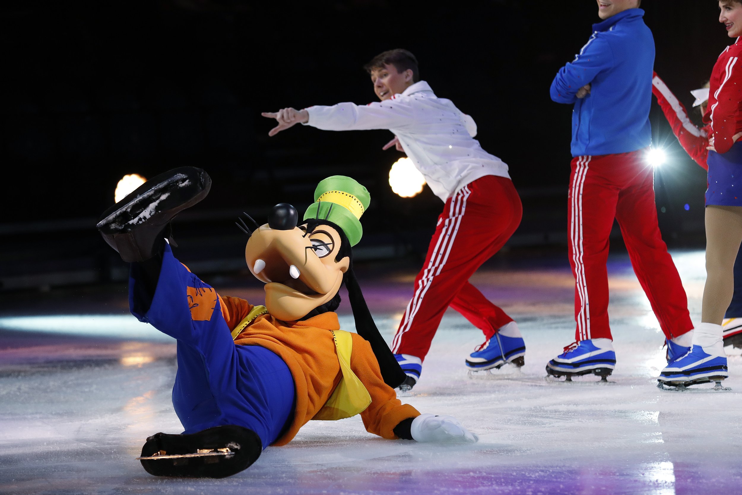 Goofy character ice skating with performers in colorful costumes on ice rink for Disney on Ice.