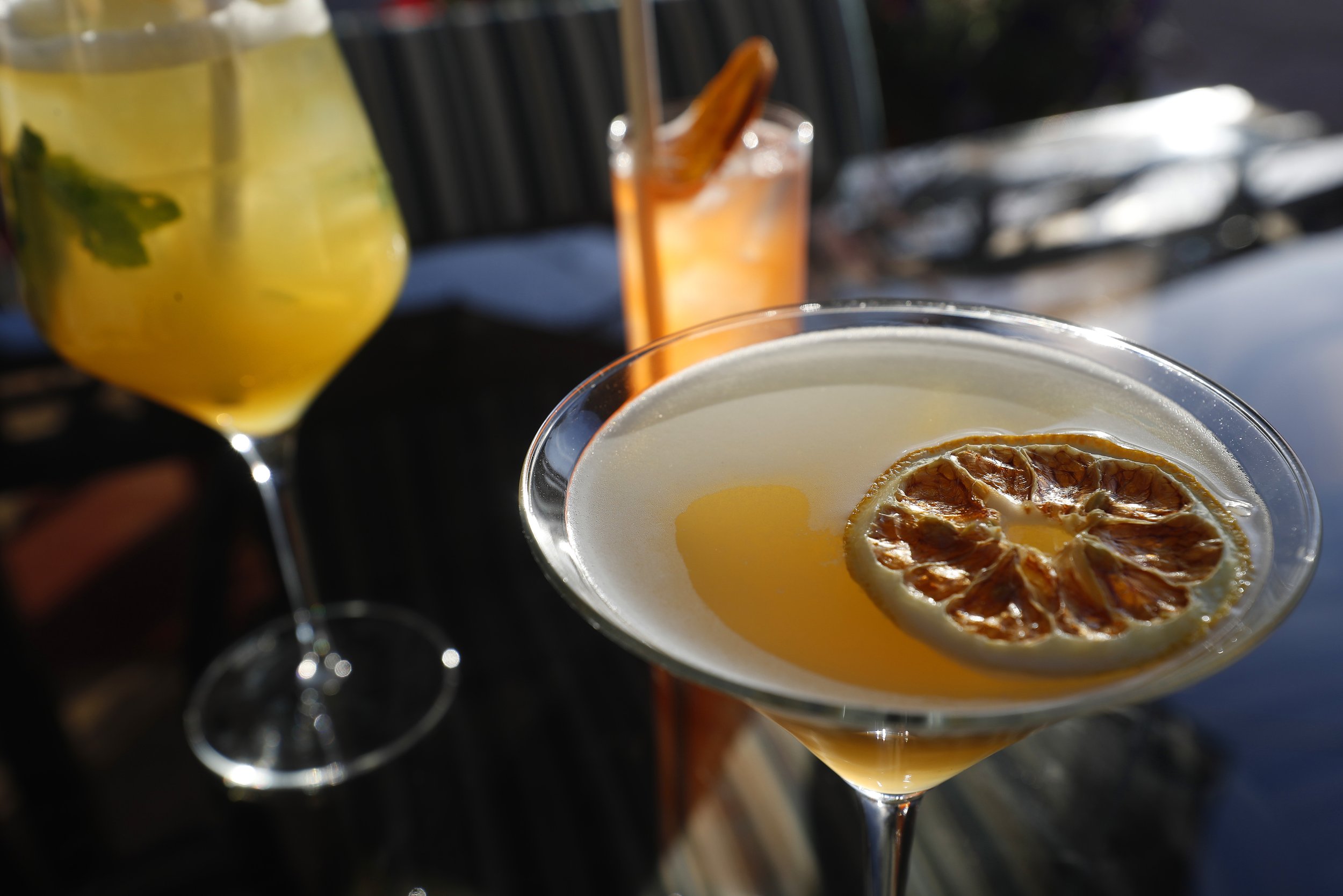 Close-up of three cocktails on a table, one with a dried citrus garnish and two others in various glassware.