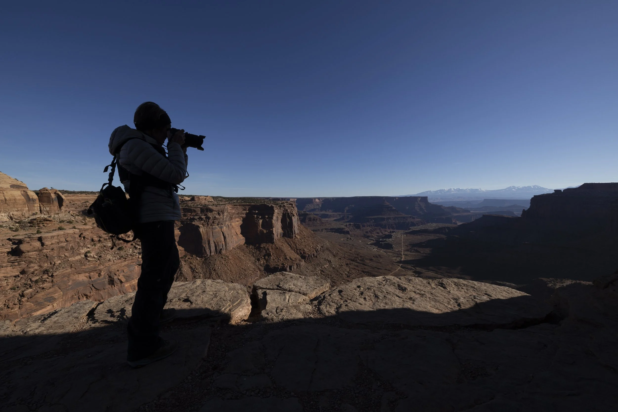 Person taking a photograph on the edge of a dramatic canyon in the Iceland Highlands during daytime, capturing the rugged volcanic landscape.