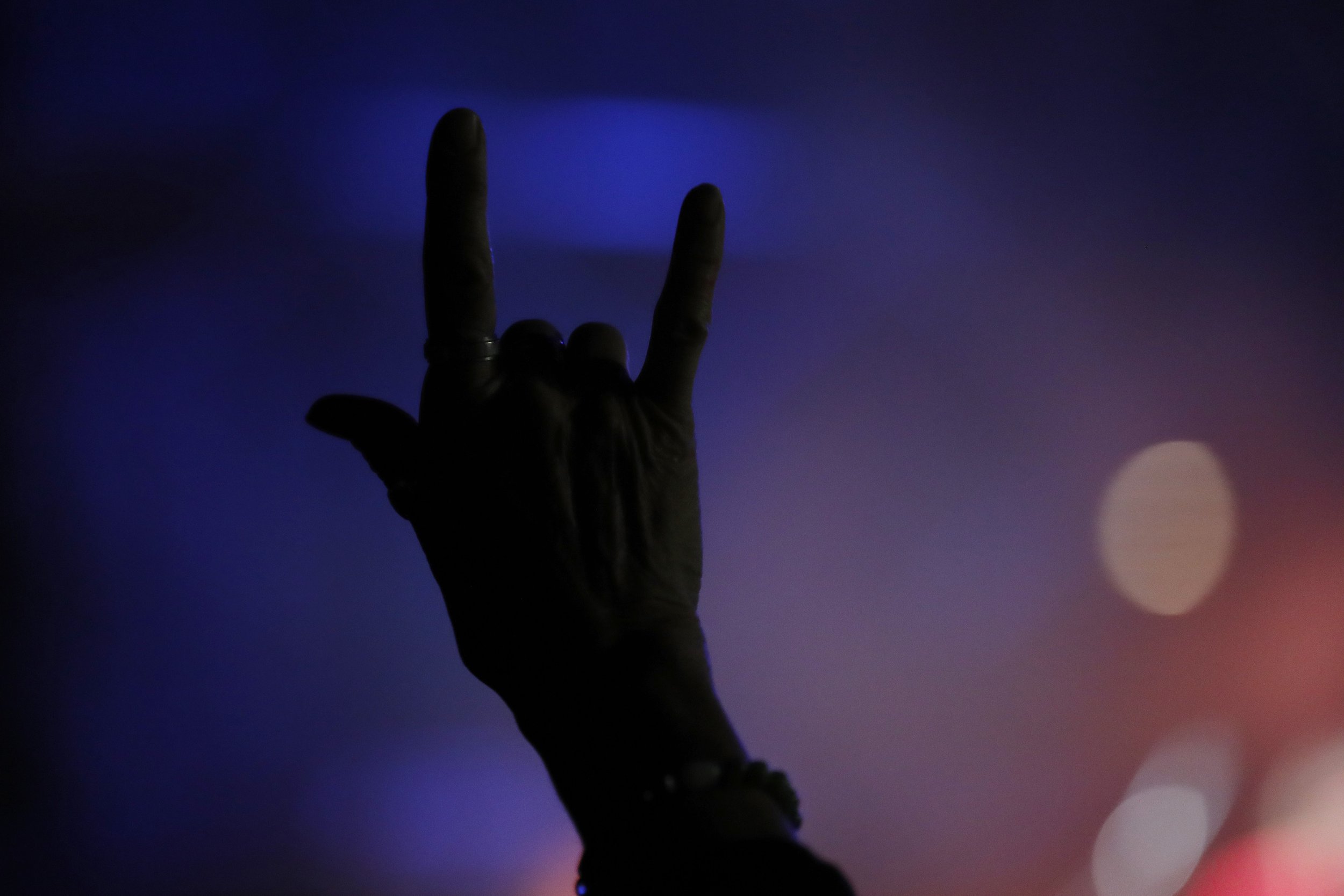 Silhouette of a hand making a rock and roll gesture against a blue and purple background during the Utah Arts Festival.
