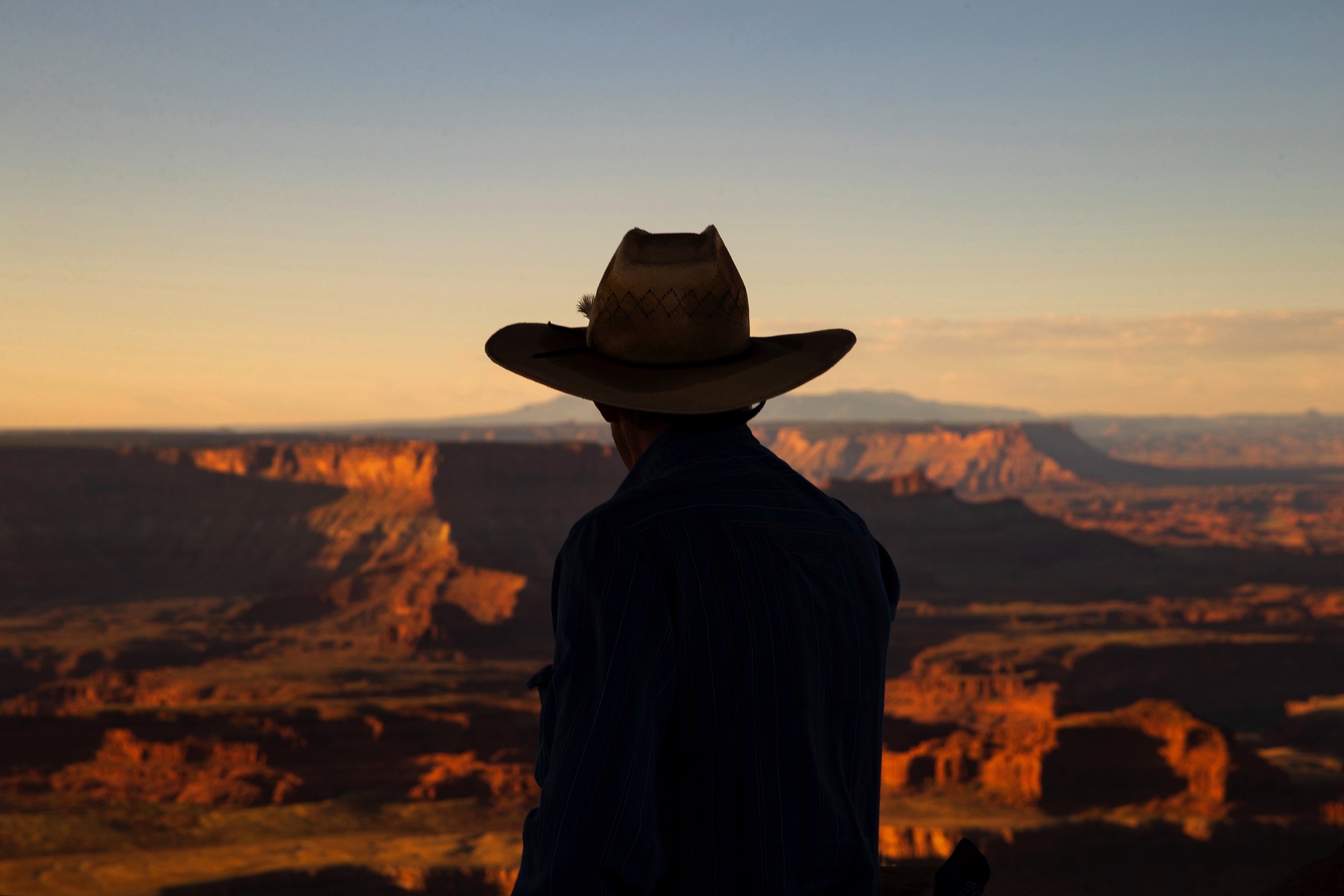 Silhouette of a person in a cowboy hat overlooking Dead Horse Point State Park at sunset.