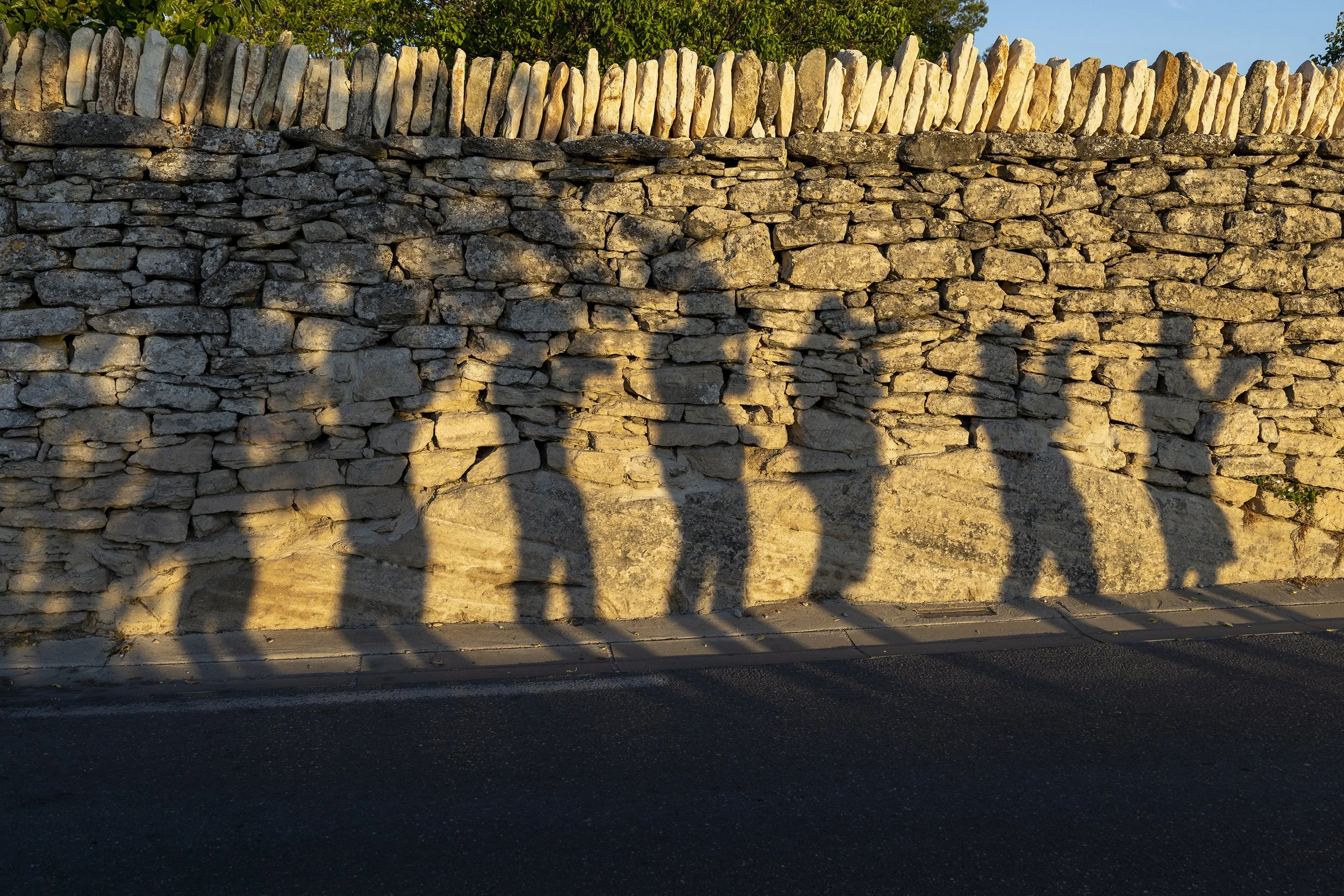 Shadows of five people cast onto a stone wall during sunset.