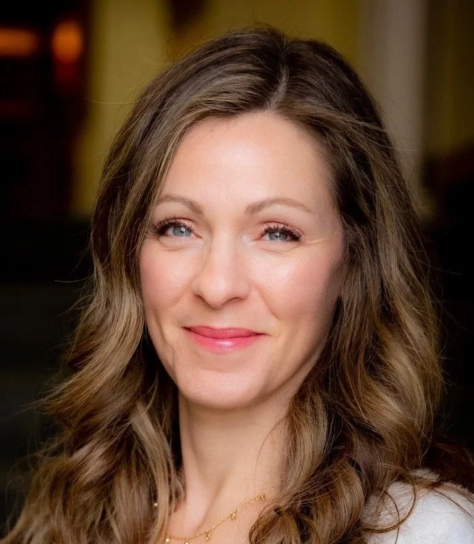 Close-up portrait of a woman with long wavy brown hair and blue eyes, smiling softly.