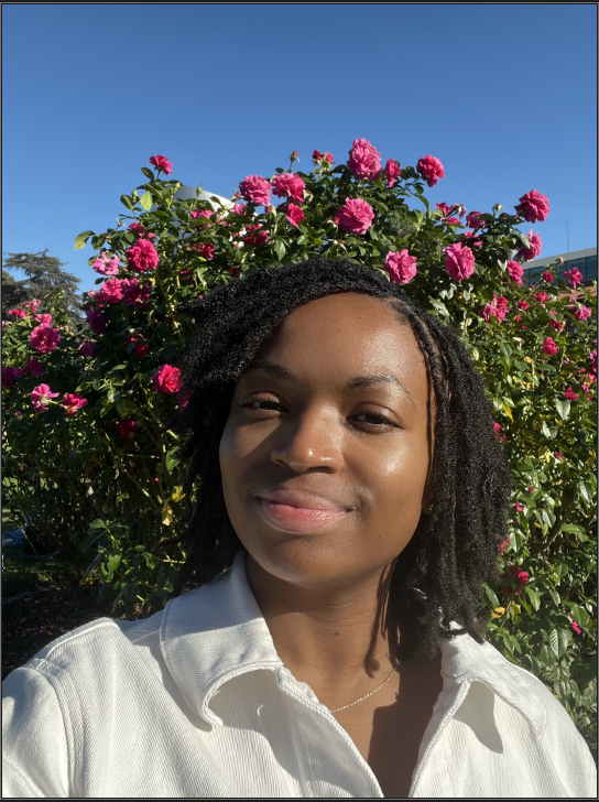 an image of Marlena Taylore smiling at the camera in front of pink flowers