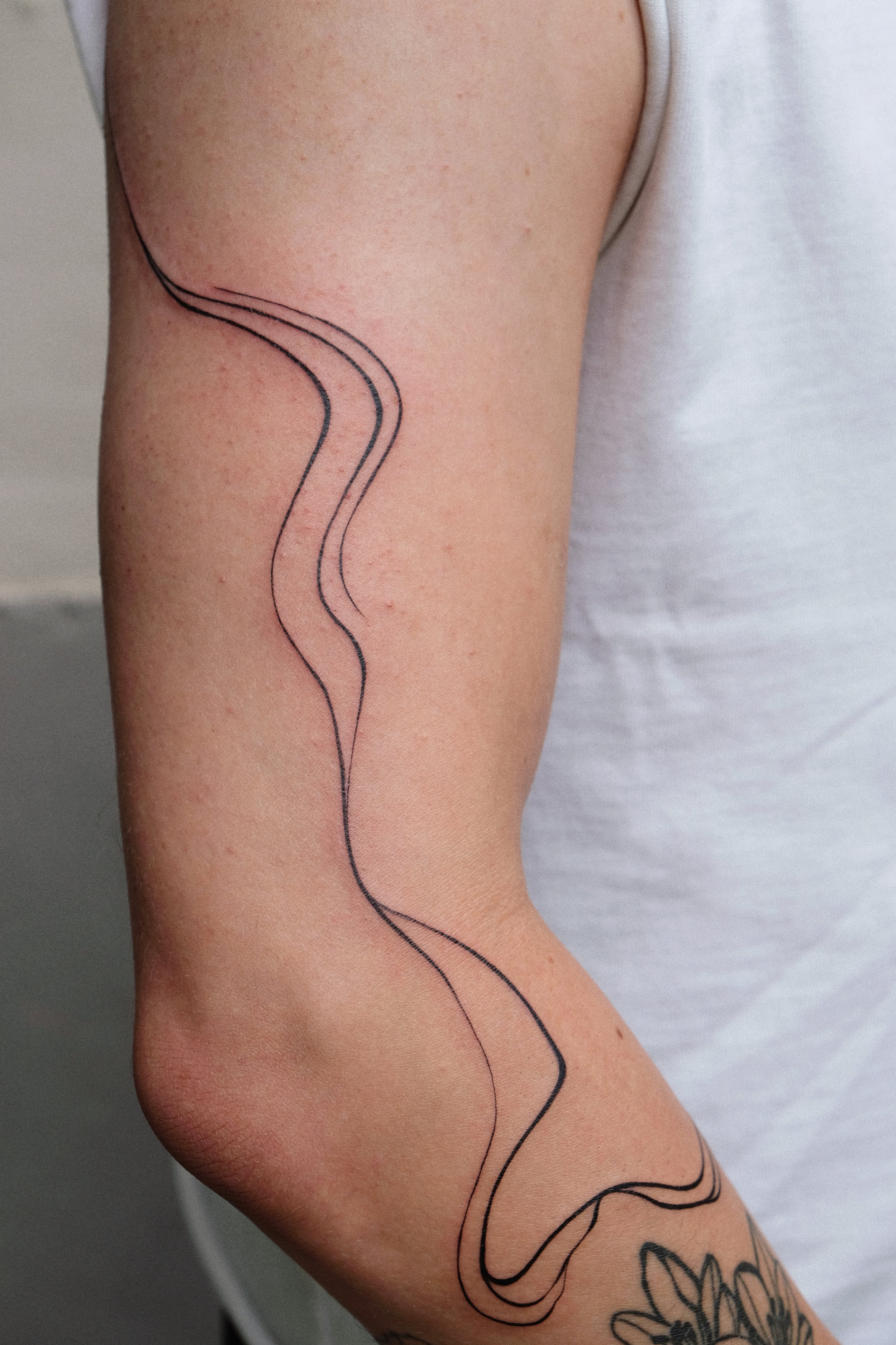 Close-up of a person's arm with a tattoo of a simple black line drawing of a long, winding snake.