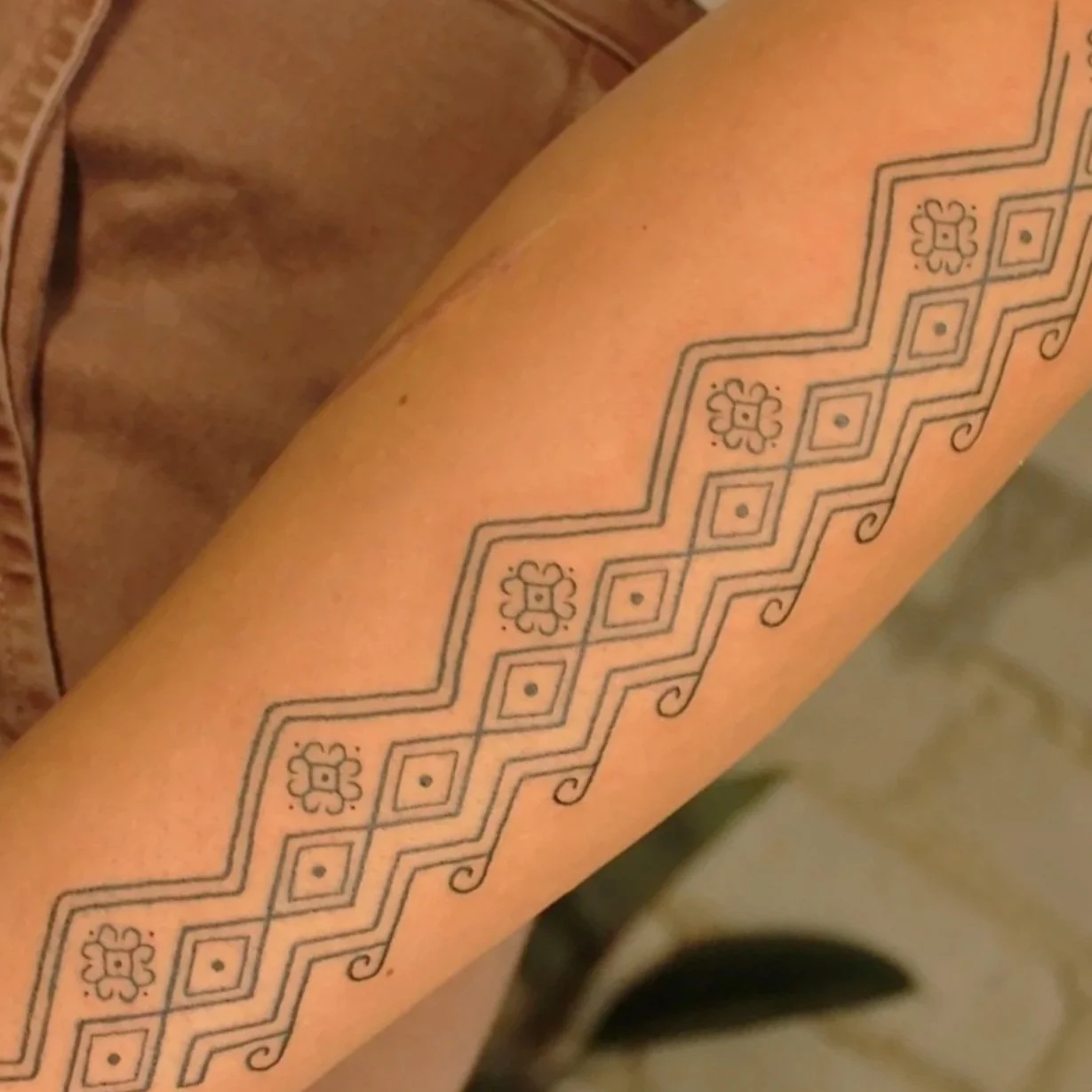 Close-up of a geometric decorative tattoo with floral motifs and curled accents on a person's arm