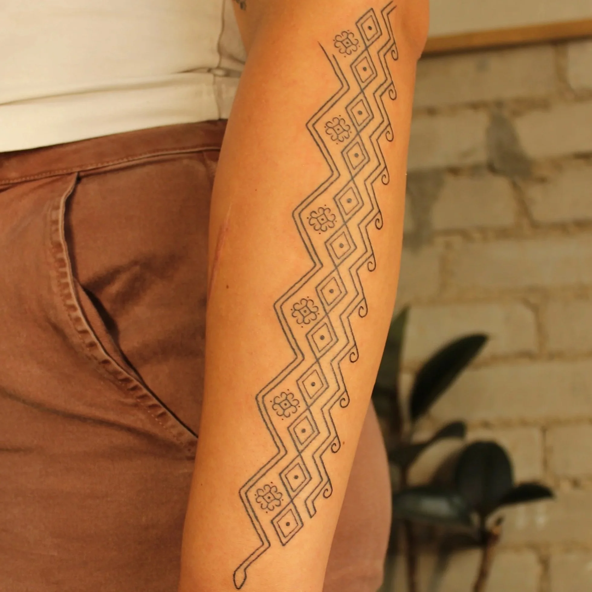 Close-up of a person's arm with a geometric tribal-style tattoo featuring linear patterns and floral motifs.