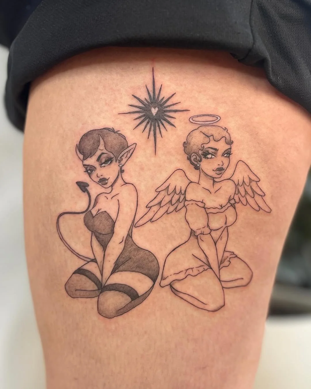 Tattoo of two stylized women with fantasy elements, one with elf ears, dark hair, and a tail, and the other with angel wings, a halo, and curly hair, with a star and heart symbol above them.
