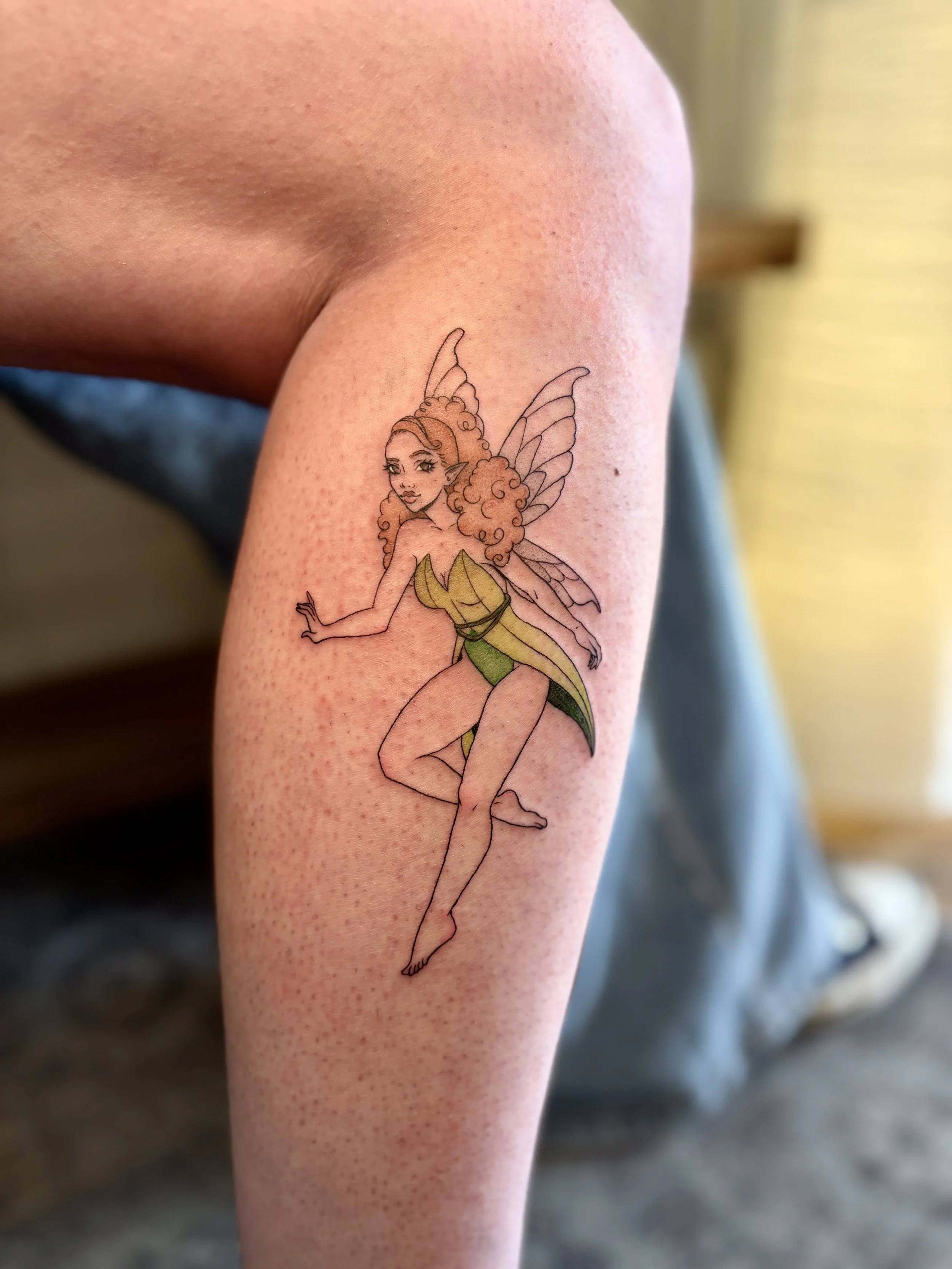 Tattoo of a fairy with curly hair, pointy ears, and butterfly wings on a person's arm.