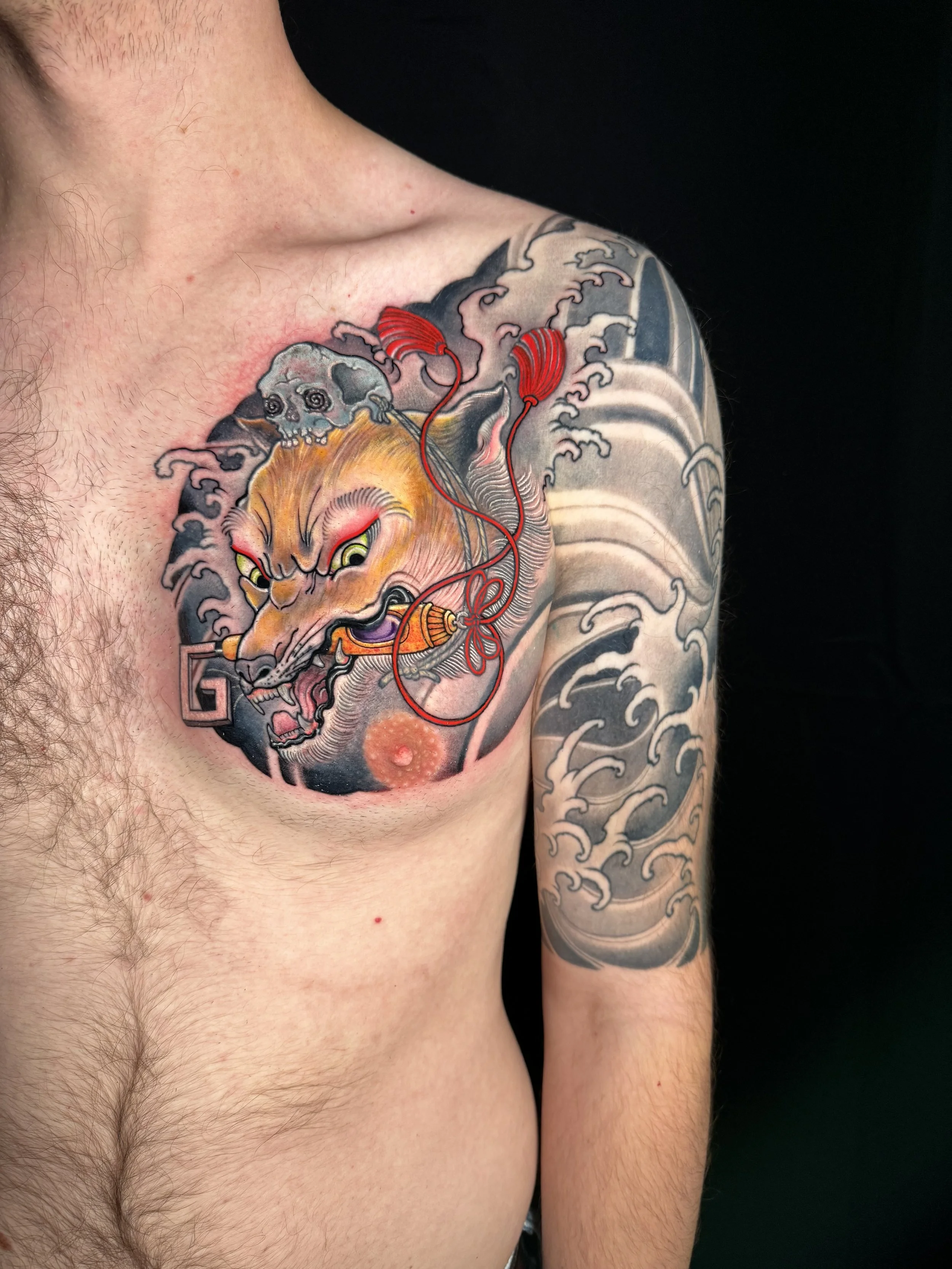 Tattoo of a tiger's head on the person's upper chest, with traditional Japanese wave design on the arm, and clouds around the tiger, using vibrant red, yellow, black, and gray colors.