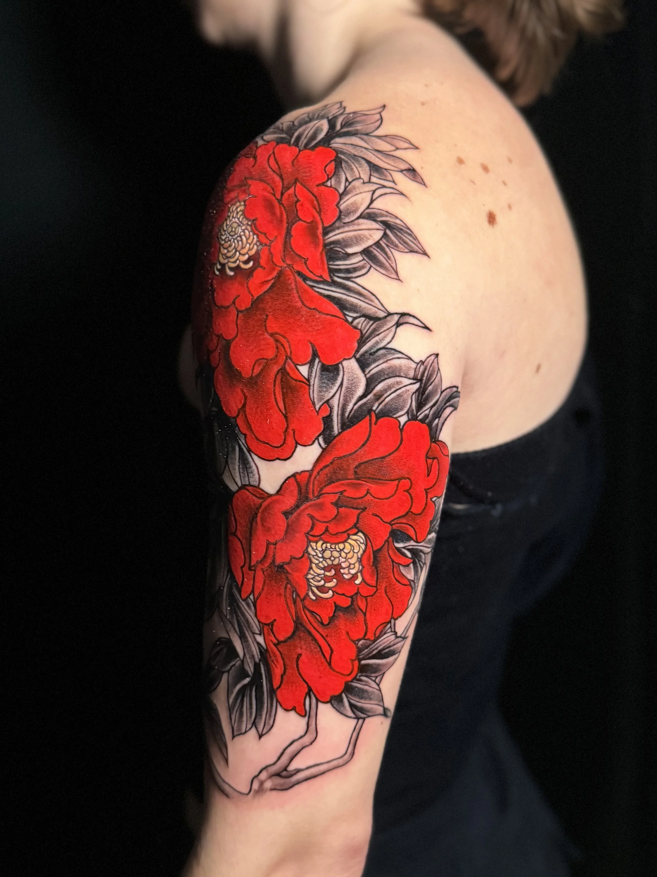 Tattoo of red peonies with black leaves on a person's upper arm