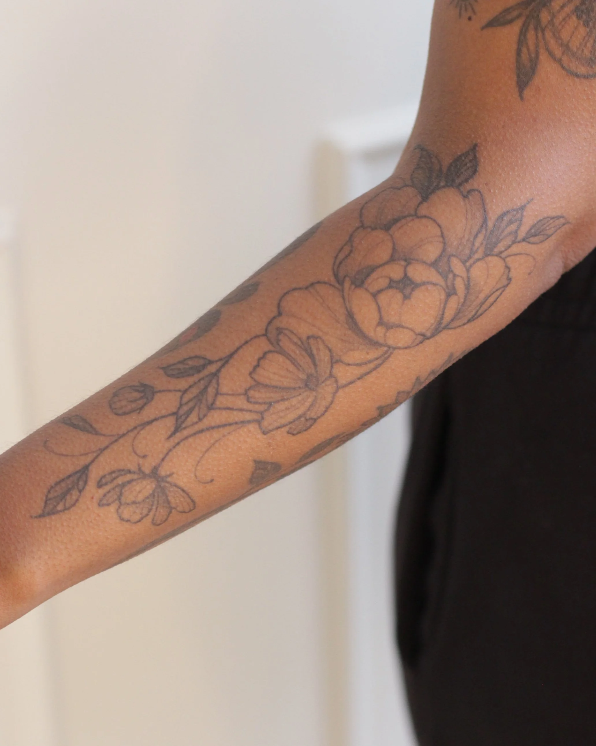 Close-up of a person's arm with a floral tattoo featuring peonies and leaves.