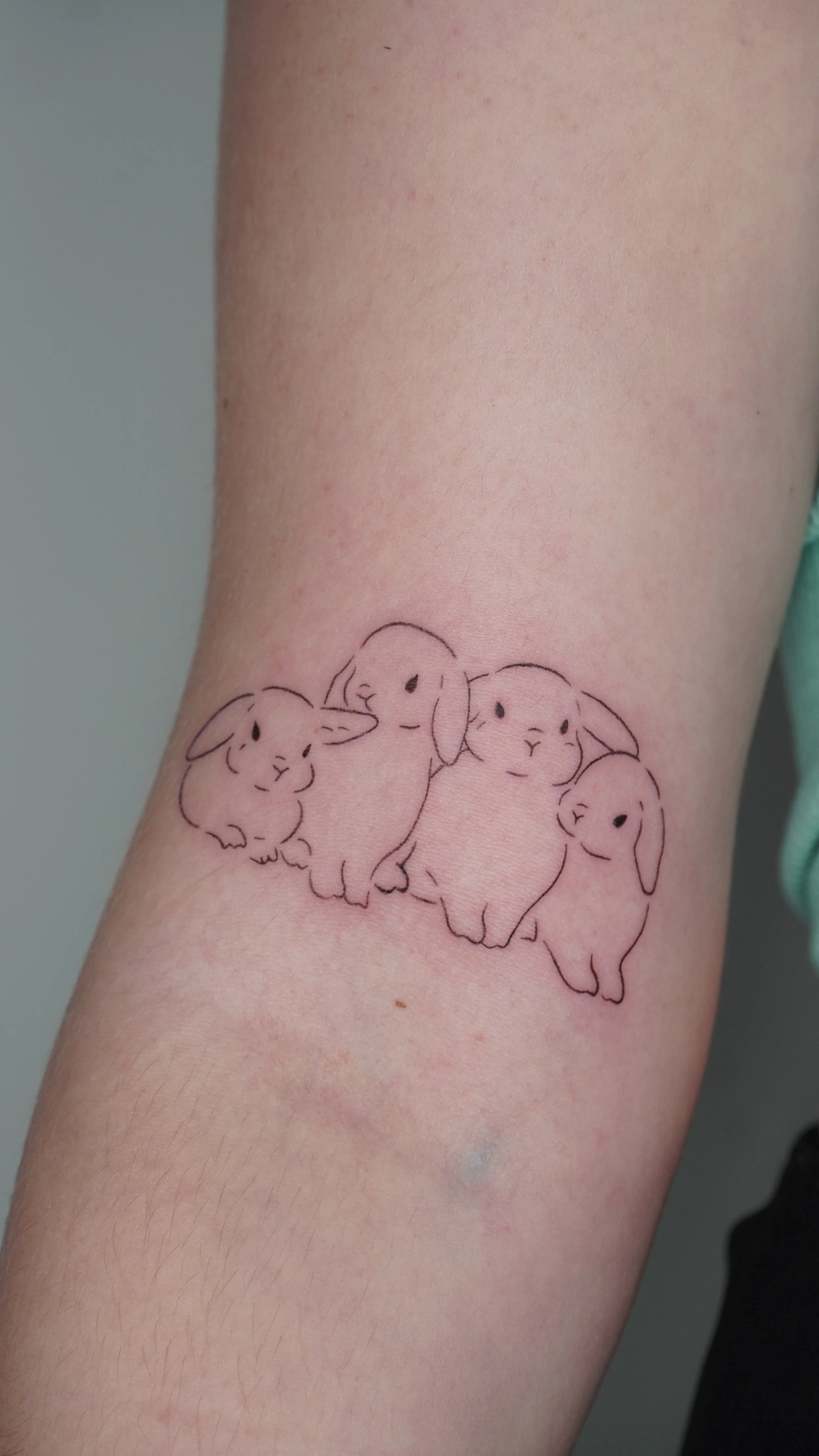 Tattoo of four cute, simple line-drawn bunnies on person's arm.