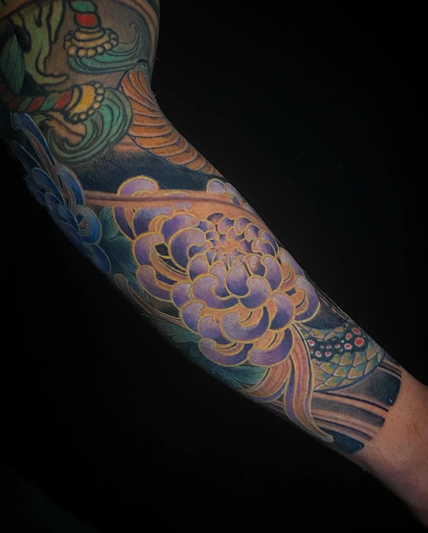 Close-up of a colorful tattoo sleeve featuring a purple flower, a yellow and green snake, and various abstract designs on a person's arm.