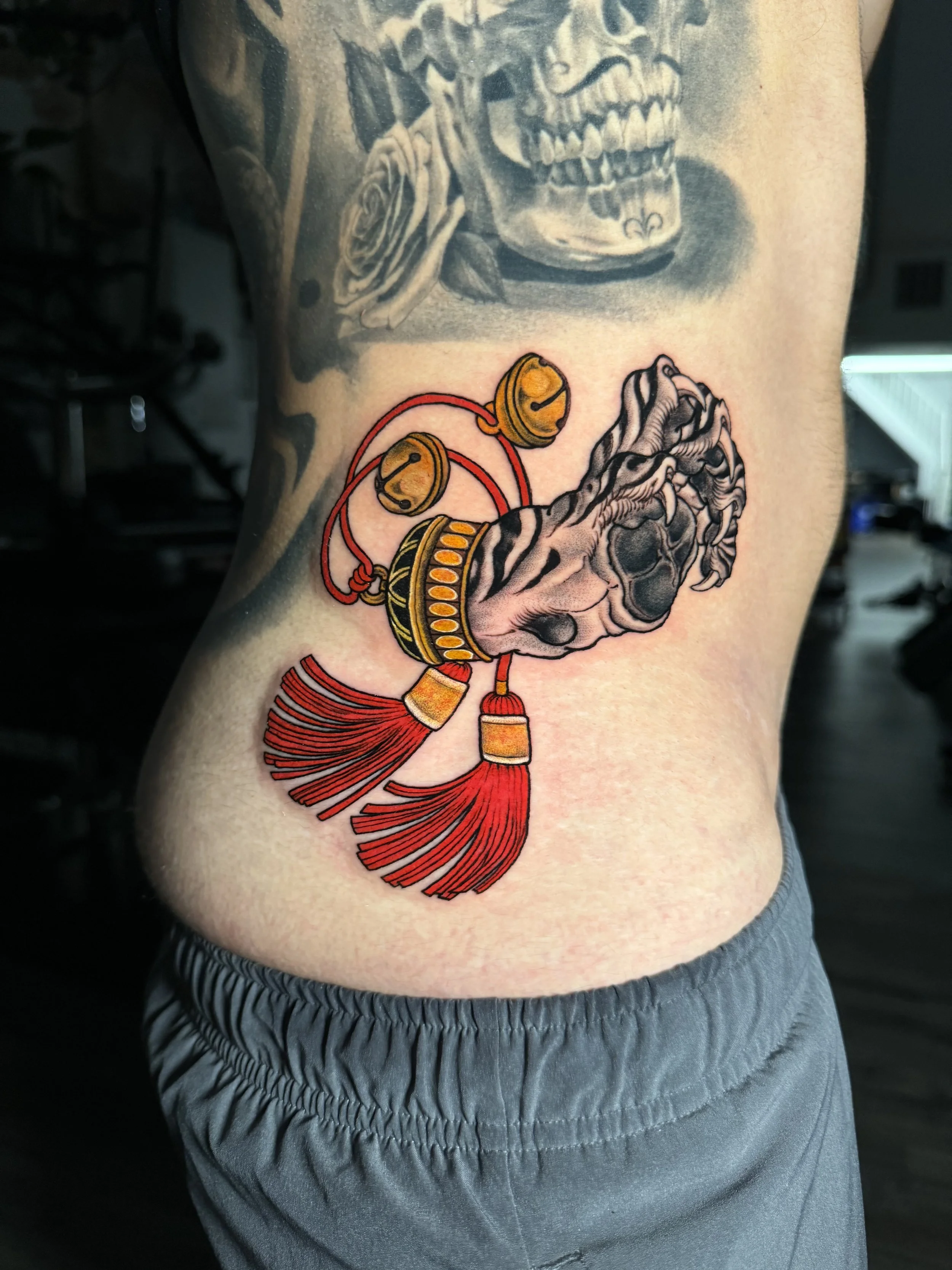 Tattoo of a hand gripping a padlock, surrounded by red and yellow decorative elements, on a person's side.