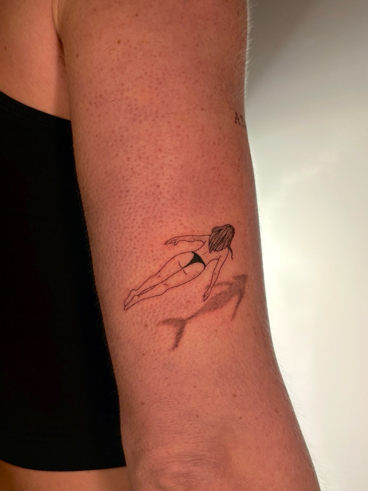Close-up of a forearm tattoo depicting a woman swimming underwater near a shadowy seabed.