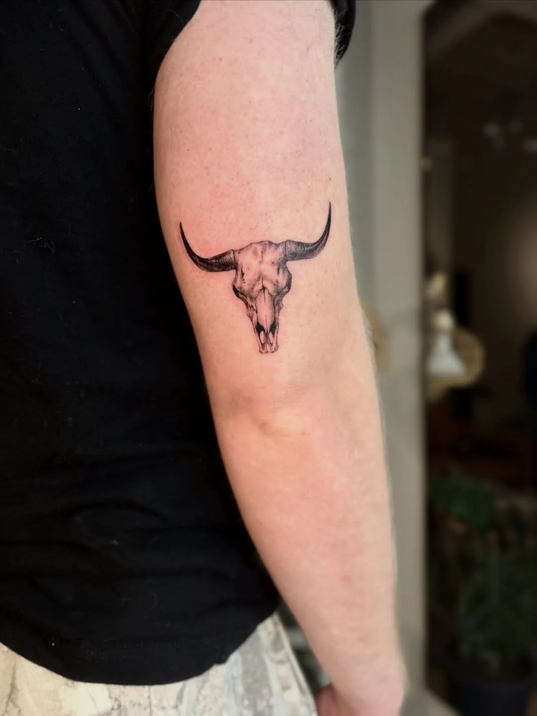 Tattoo of a longhorn cow skull with horns on a person's upper arm.