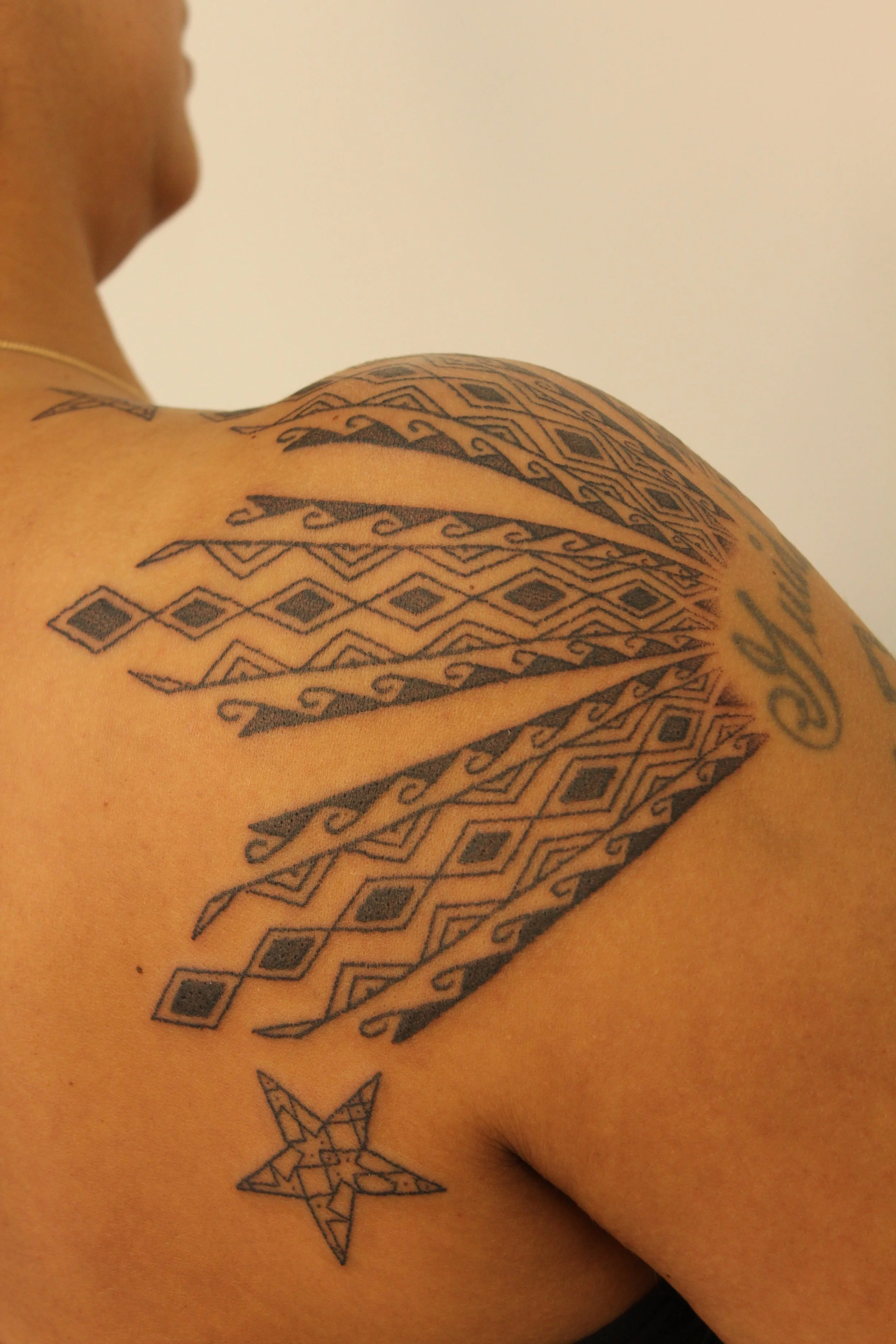 Close-up of a person's shoulder and upper arm with intricate black geometric tattoos, including a star and various patterns.