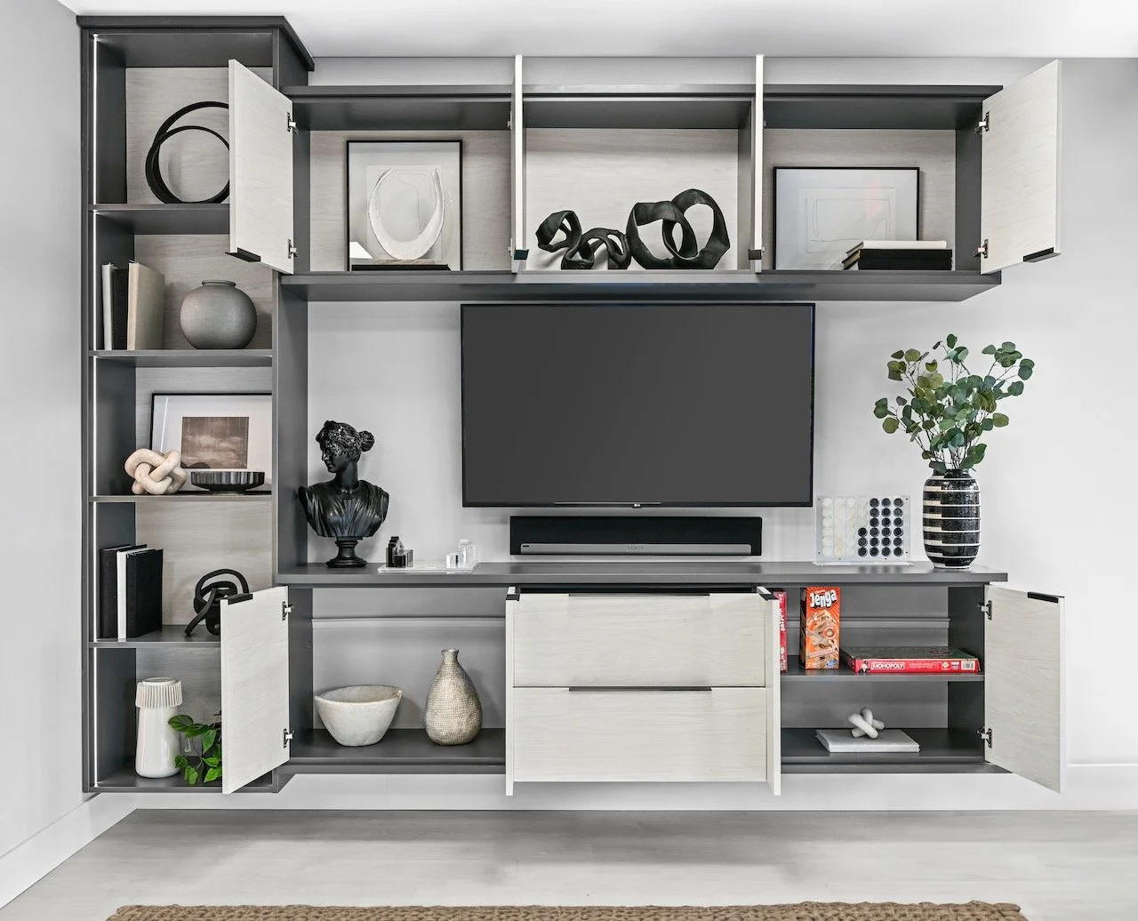 Modern wall-mounted entertainment center with open and closed shelving, a flat-screen TV, decorative items, and a potted plant.