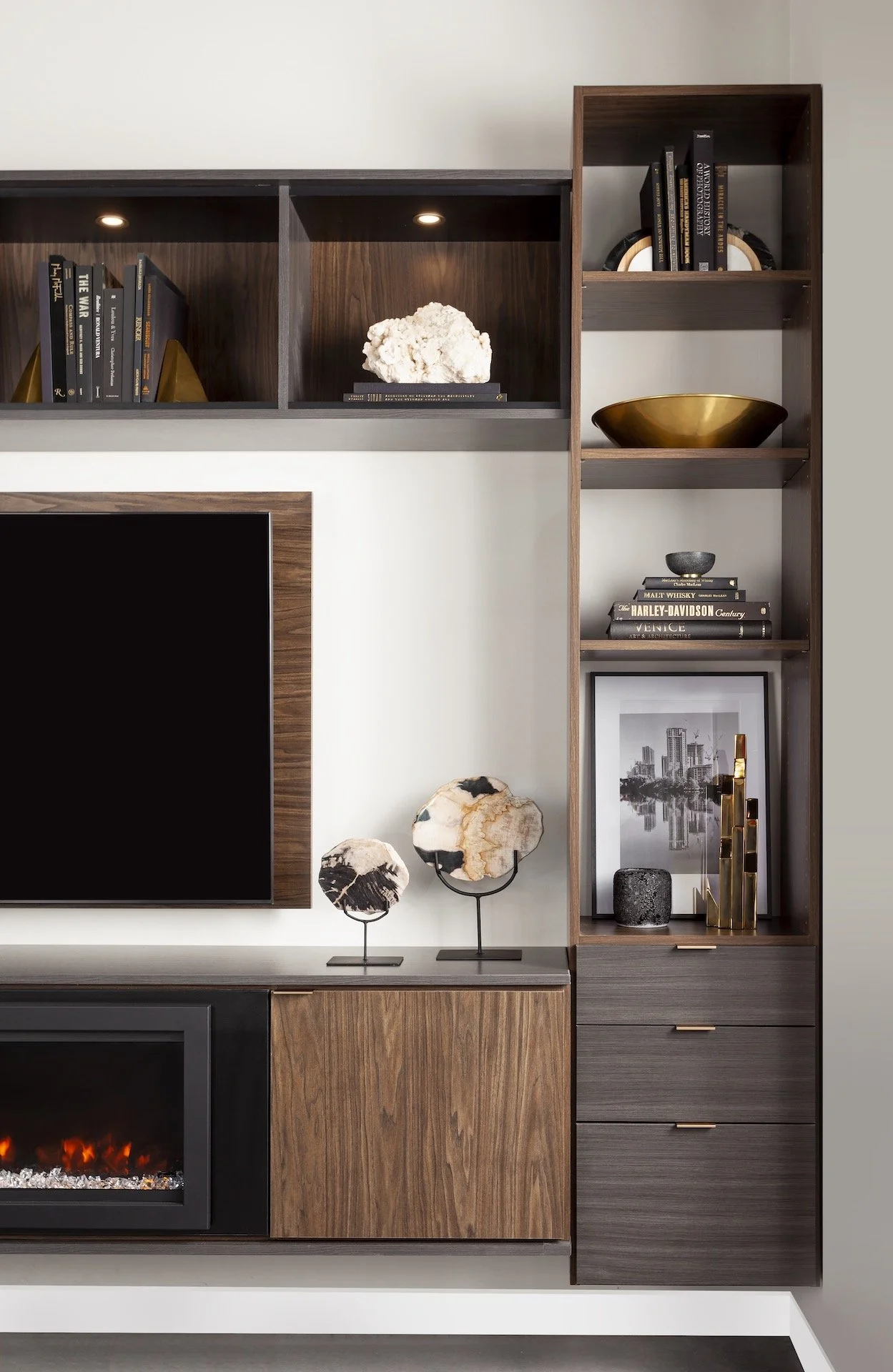Modern wooden entertainment center with books, decorative objects, and framed photo, with an electric fireplace underneath.