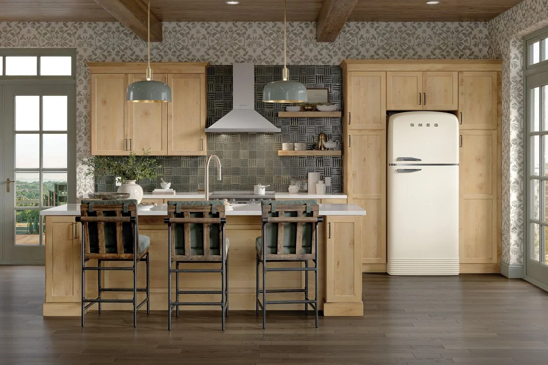 Bright kitchen with light wooden cabinets, a white refrigerator, two hanging pendant lights, a white countertop with a sink, black and gray tiled backsplash, bar stools at the island, and large glass doors letting in natural light.
