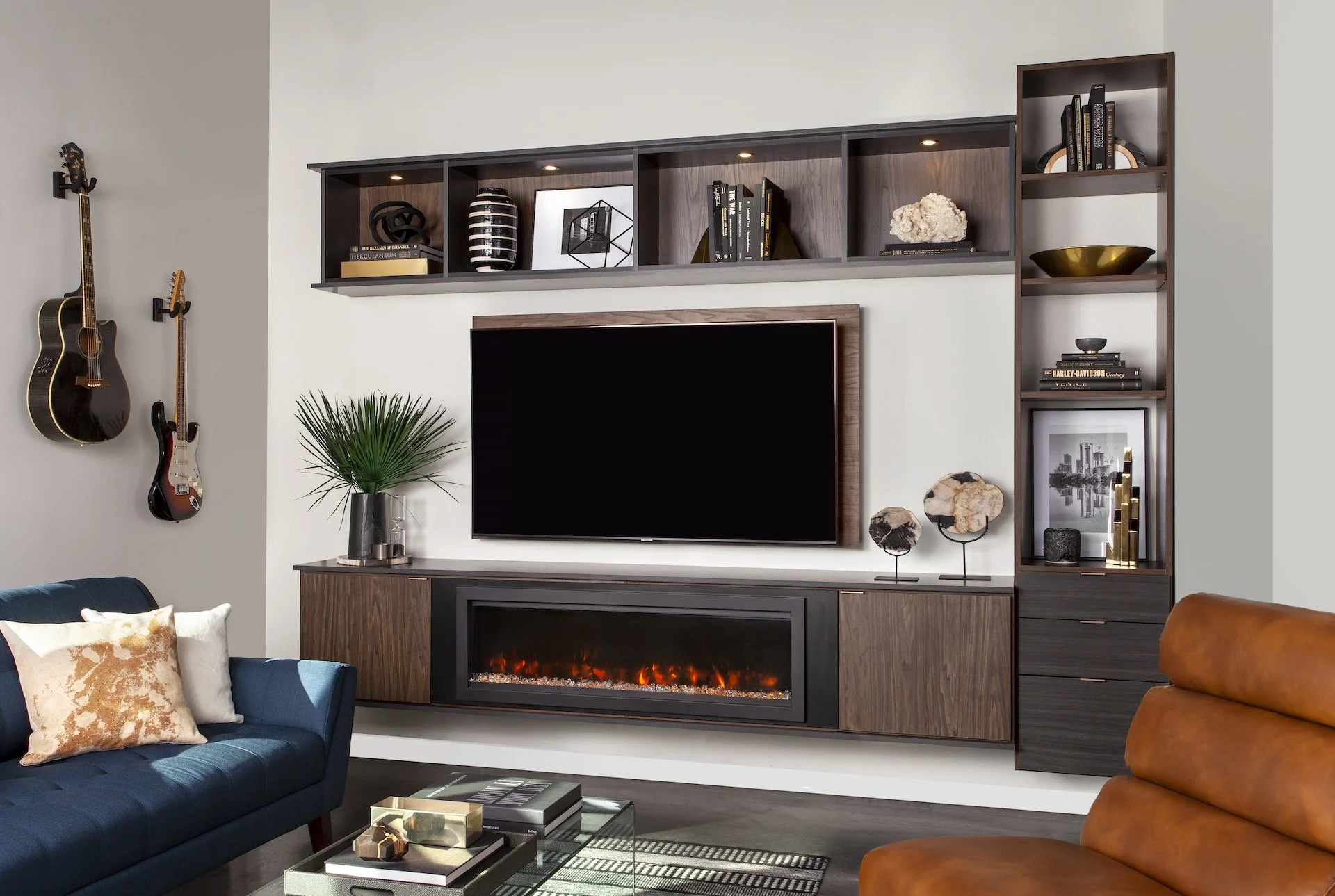 Modern living room with a wall-mounted flat-screen TV and electric fireplace console, surrounded by dark wood shelves and decorative items, including books, plants, and art.