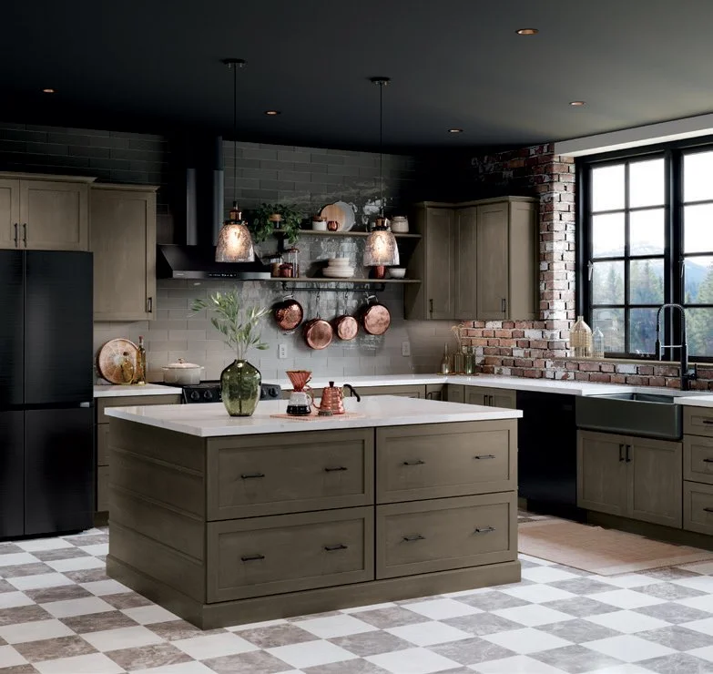 Modern kitchen with gray cabinets, black refrigerator, white countertop island, exposed brick wall, large window, gray tile backsplash, hanging pendant lights, open shelves with dishes and plants, checkered flooring.