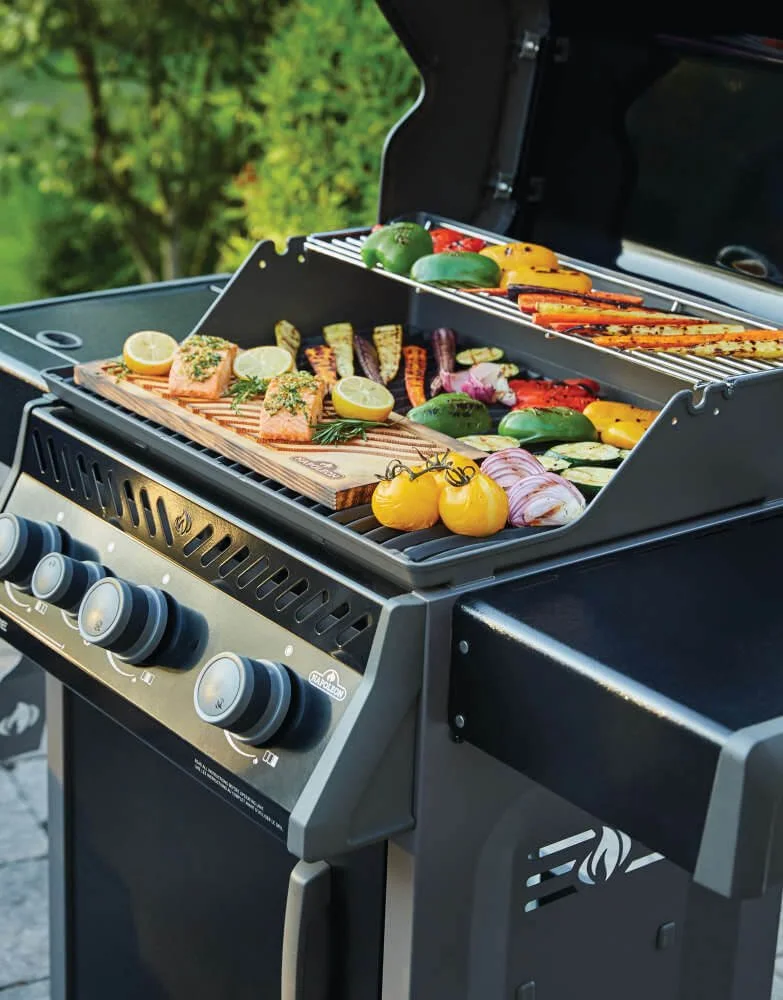 Grill with salmon fillets, lemons, and fresh vegetables cooking outdoors.