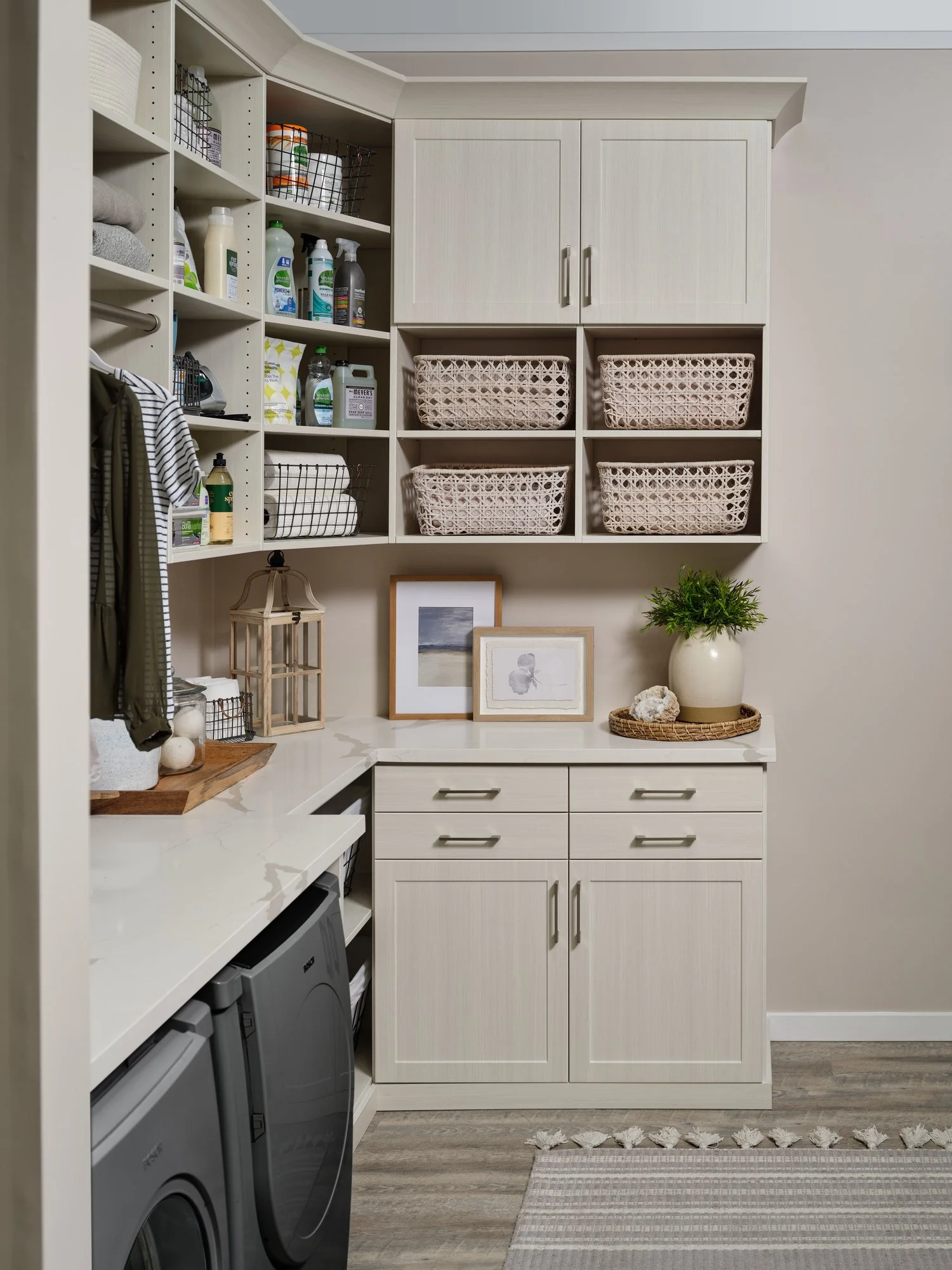 A well-organized laundry room with bright natural open shelving containing cleaning supplies, baskets, and decorative items, along with a countertop and a front-loading washing machine and dryer.