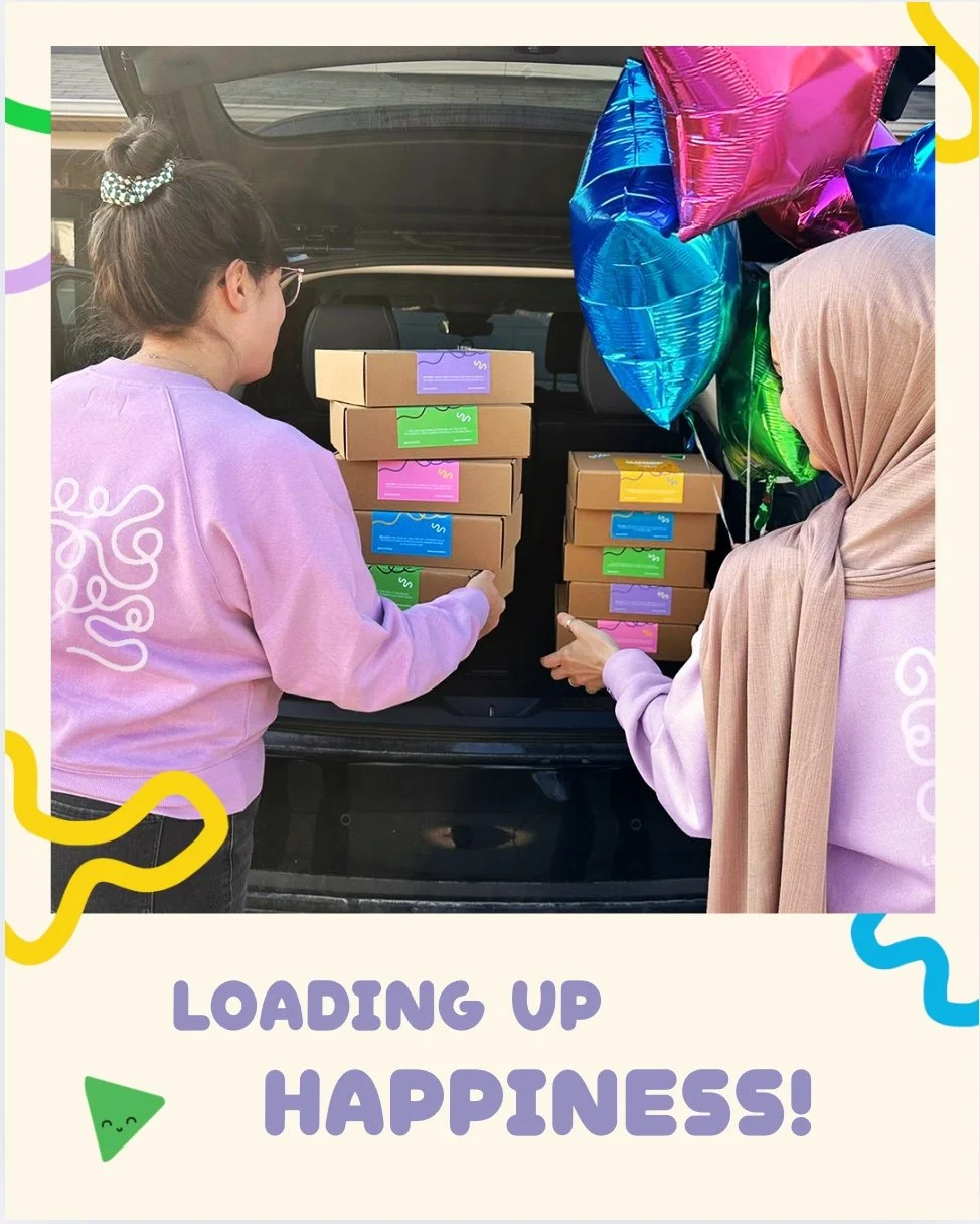 Two women loading colourful craft kits and balloons into the trunk of a car. The photo has a caption that says 'Loading Up Happiness!'.