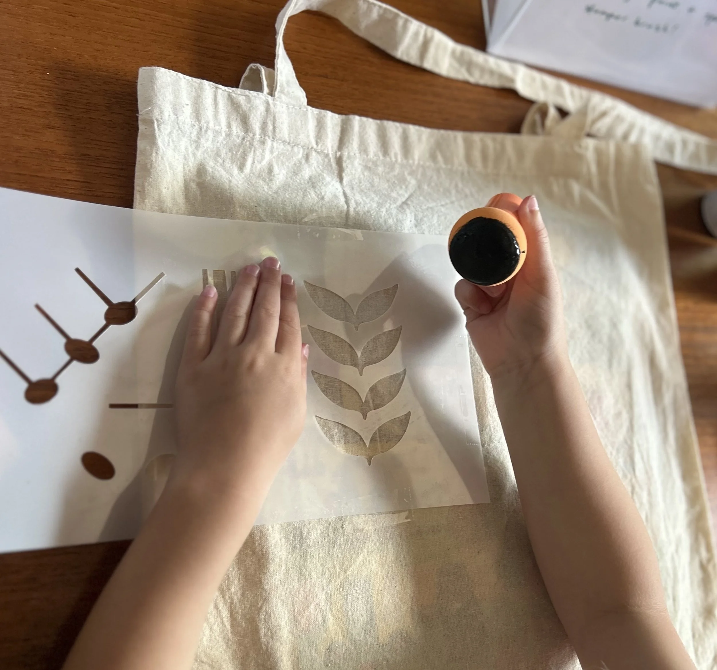 Children's hands working on a craft project with a stencil and a stamp on a table.