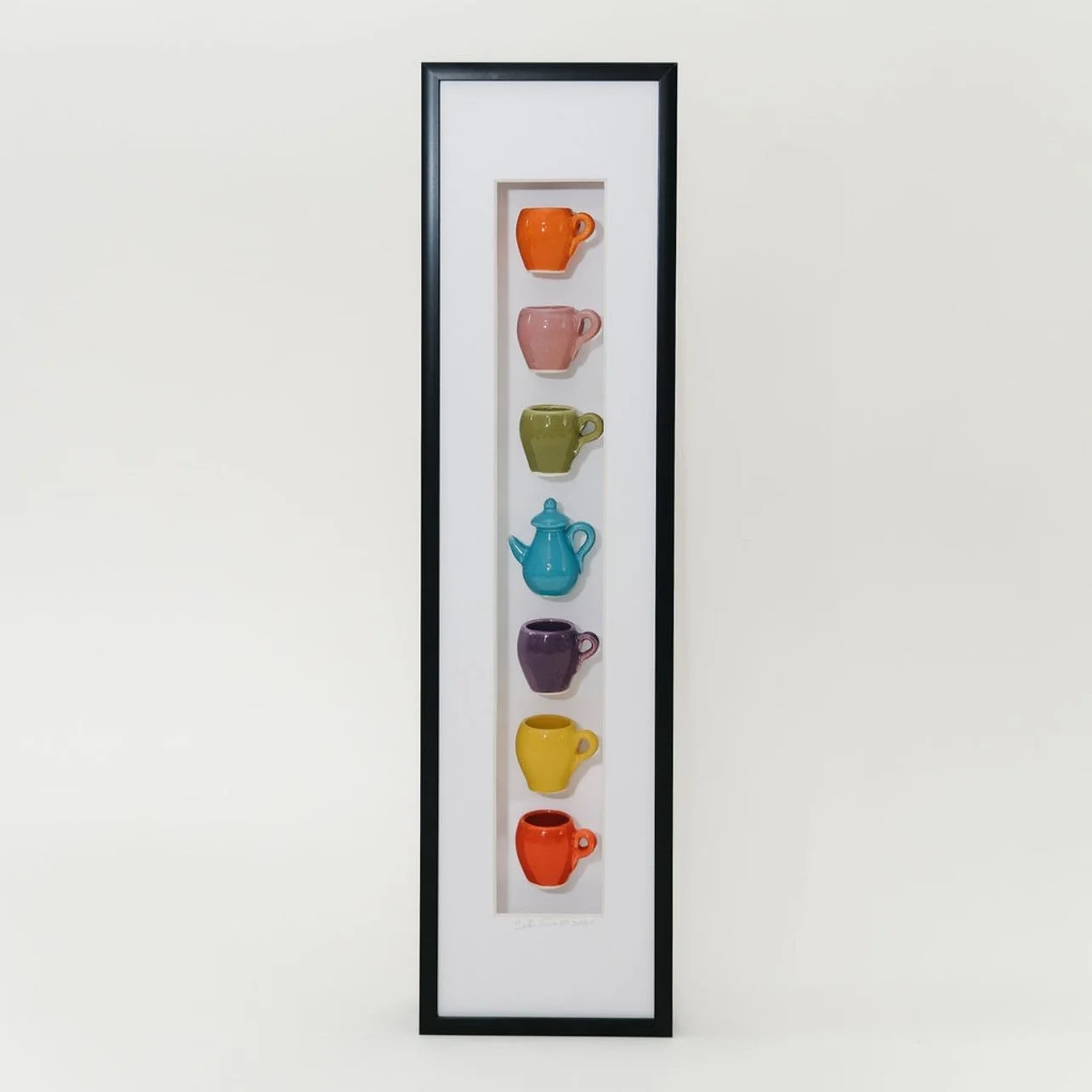A framed piece of seven colorful mugs  and one teapot in the center mounted vertically.