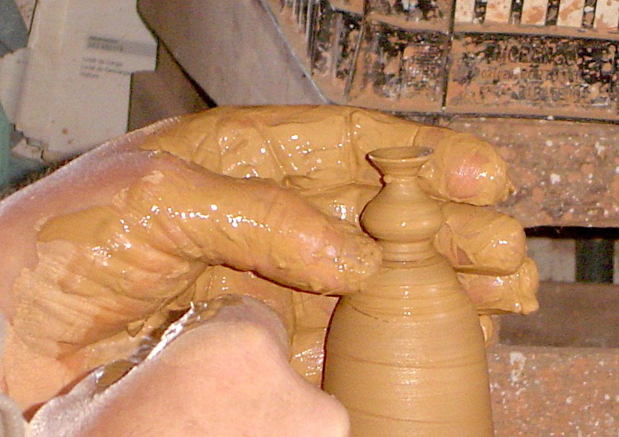 Close-up of a person's hand shaping a small clay vase on a pottery wheel.