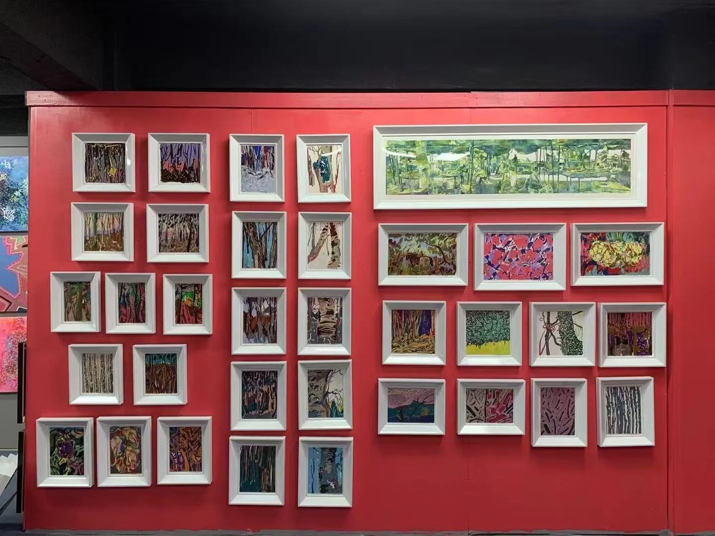 Gallery wall with multiple framed abstract and landscape paintings, arranged on a red wall.