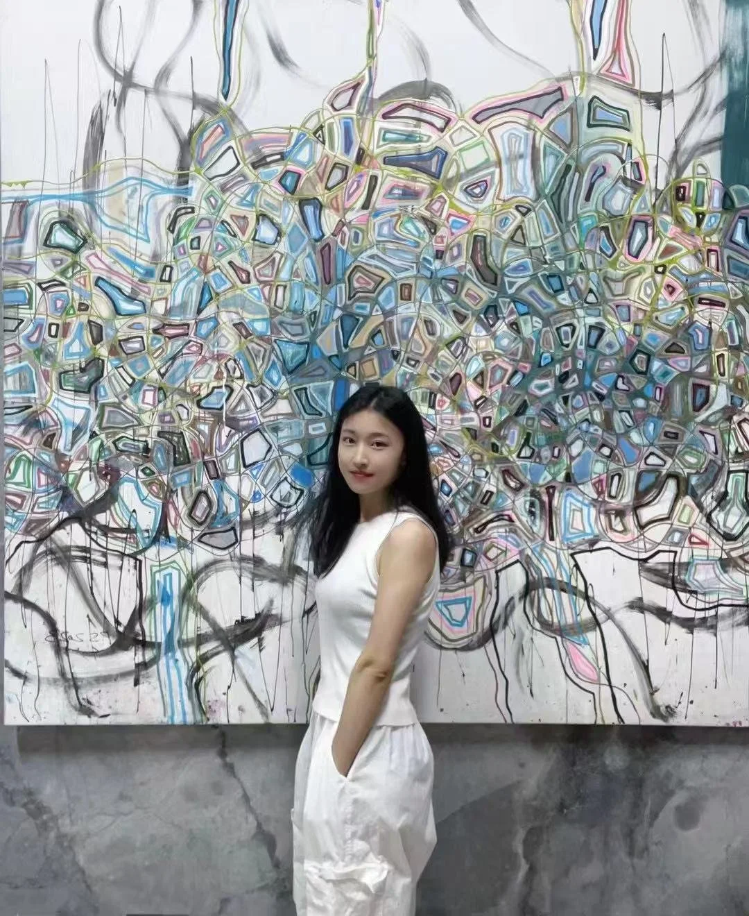 Young woman in a white dress standing in front of a colorful abstract street art mural in an indoor gallery.