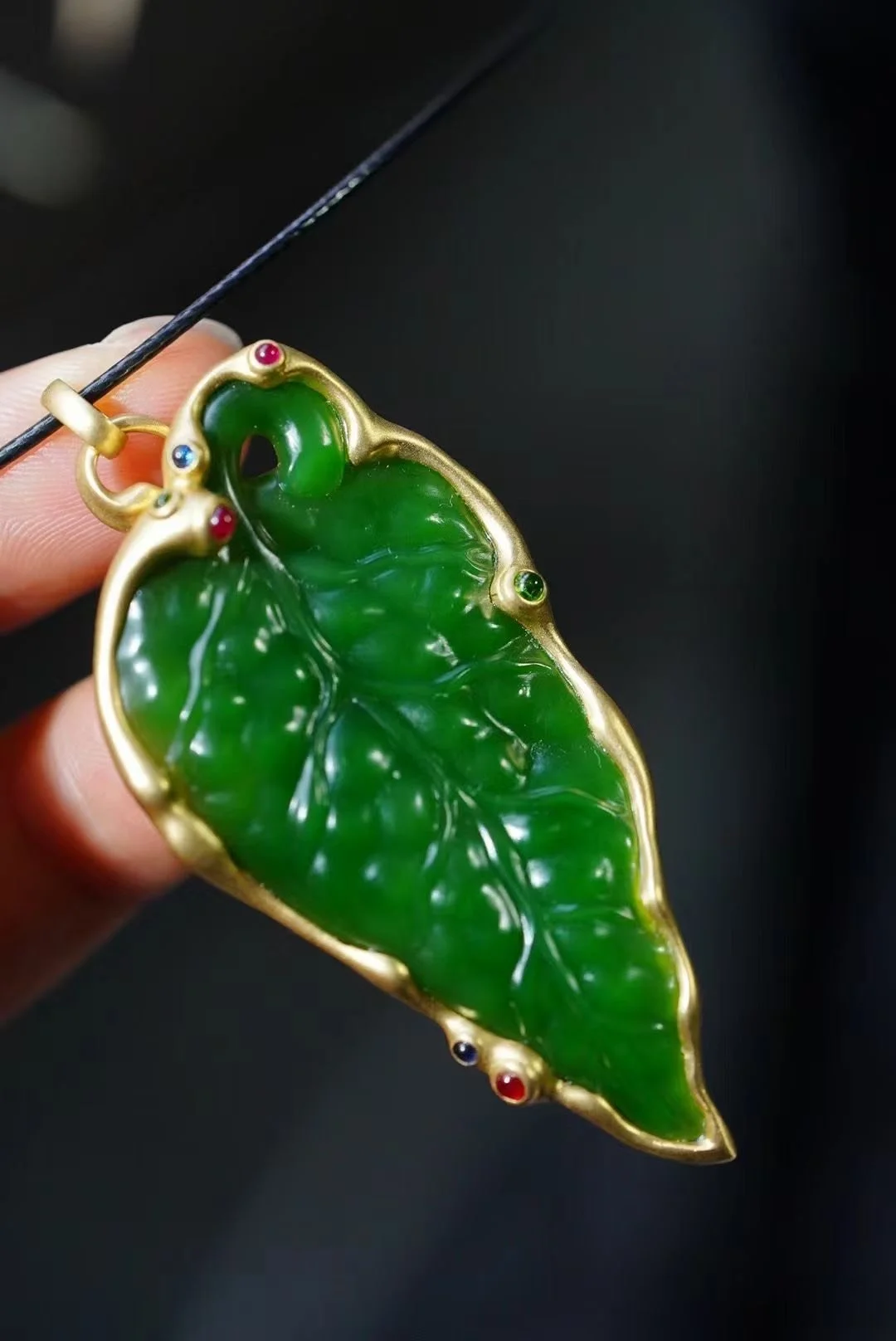 Green jade pendant in gold setting with small colored gemstones.