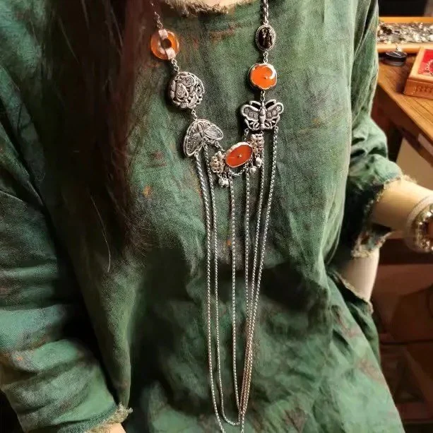 A person is wearing a long necklace with various charms, including a butterfly, a ladybug, and orange beads, over a green, patterned garment.