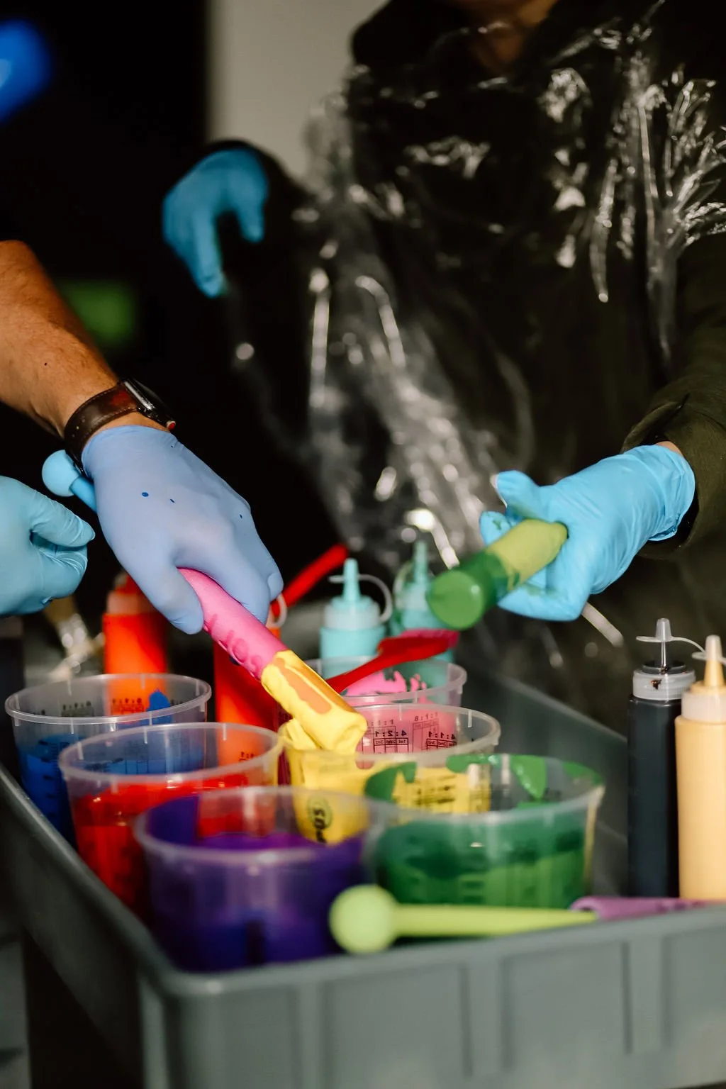 Pouring colorful liquid dye into cups for tie-dye fabric at a craft station.