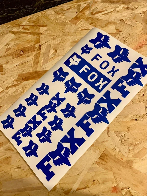 Sheet of blue and white stickers with fox illustrations and the word "FOX" written on some, placed on a wooden surface.