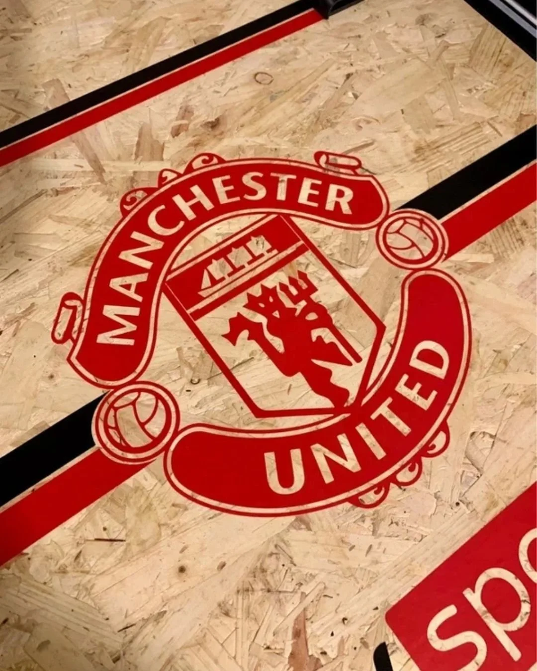 Manchester United logo on a wooden surface with red and black lines.