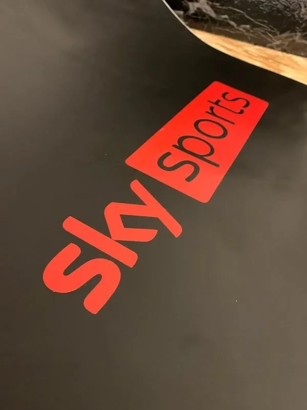 Red sticker with black text that reads 'sky SPORTS' on a black surface, likely a table or desk.
