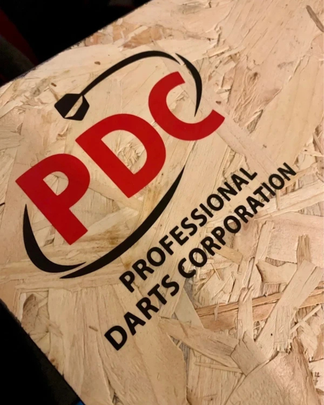 A sticker with the logo 'PDC' in red and black, featuring a wire cutter or pliers above the text, placed on a wooden surface. The text 'PROFESSIONAL PARTS CORPORATION' is written below in black.