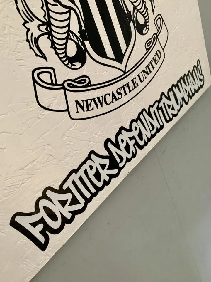 Black and white logo with a crest and banner that reads 'Newcastle United' and text that says 'Football Premier League' on a textured white wall.
