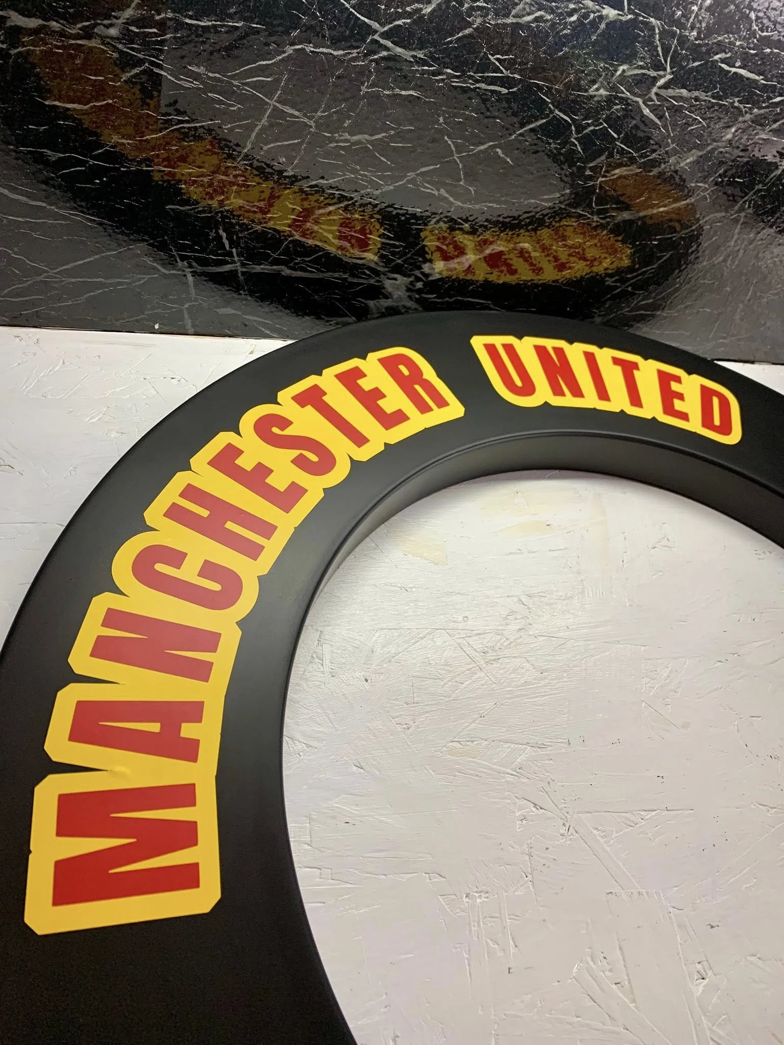 Close-up of a large black sign with bold yellow and red text that reads 'WARNING: DASIED UNITED' against a white textured wall background.