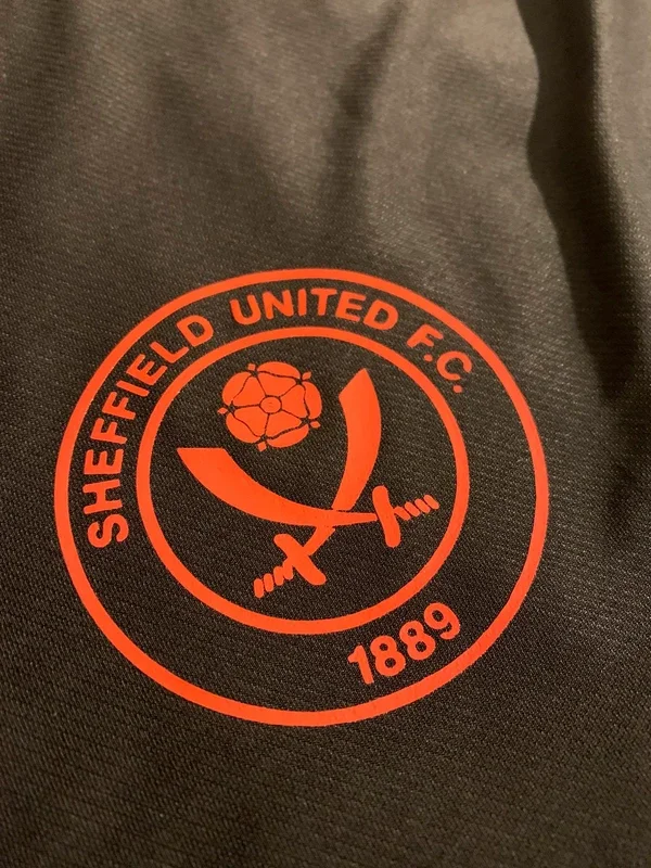 The emblem of Sheffield United F.C. featuring a red circular logo with a flower and two swords crossed at the center, and the year 1889.