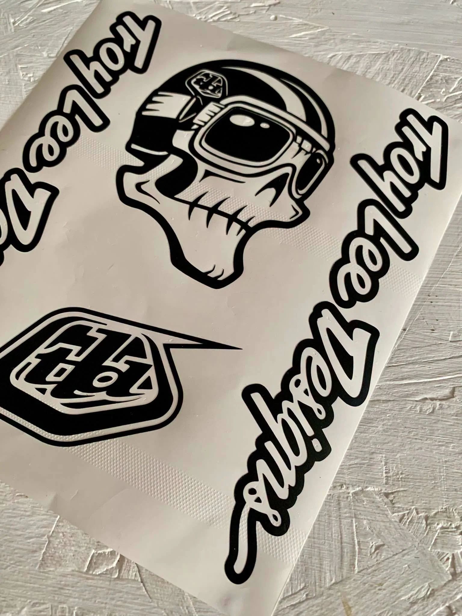 Black and white sticker with a skull wearing a ski helmet and goggles, and a stylized cursor hand pointing at the skull. The sticker has the repeated phrase 'Hey ho!' around the skull.